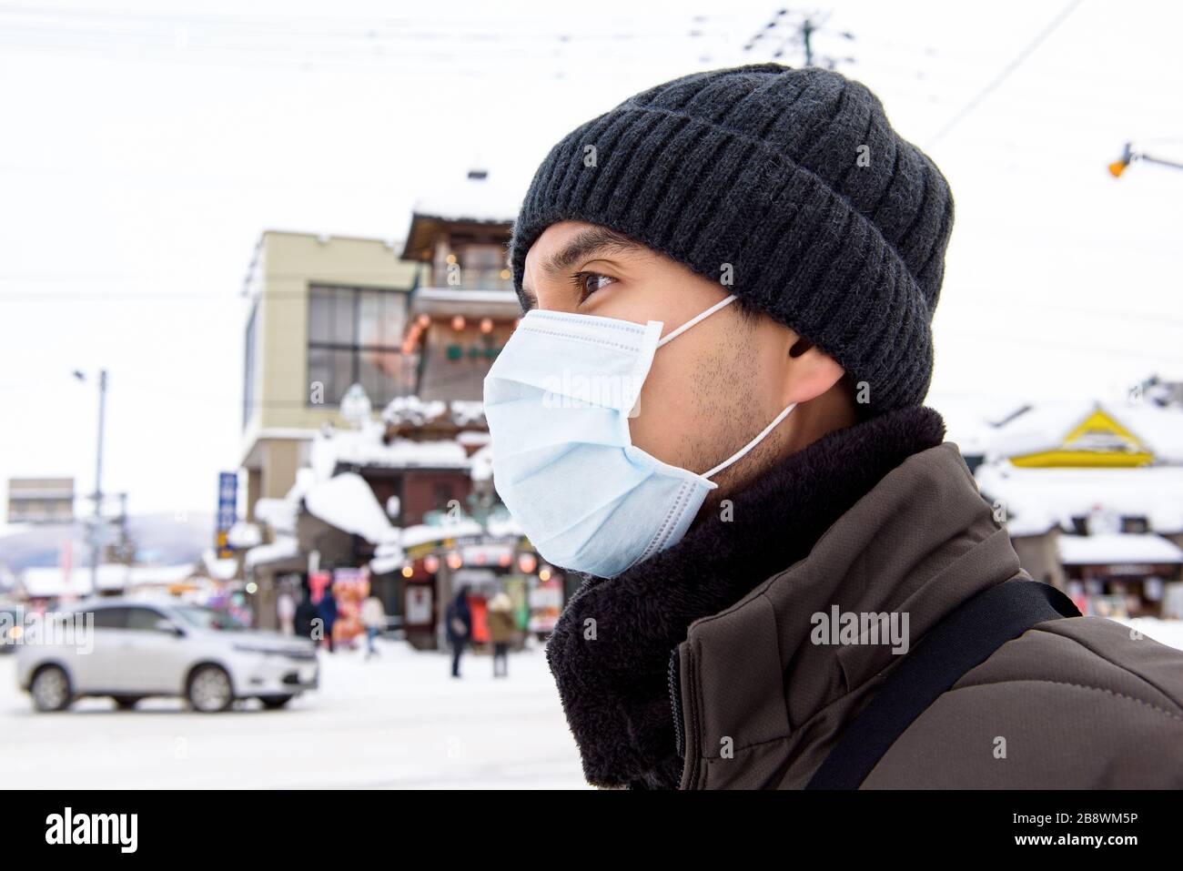 Asiatischer Tourist, der eine Maske trägt, die Coronavirus schützt, während er im Winter im Freien in Hokkaido-Japan spaziert Stockfoto