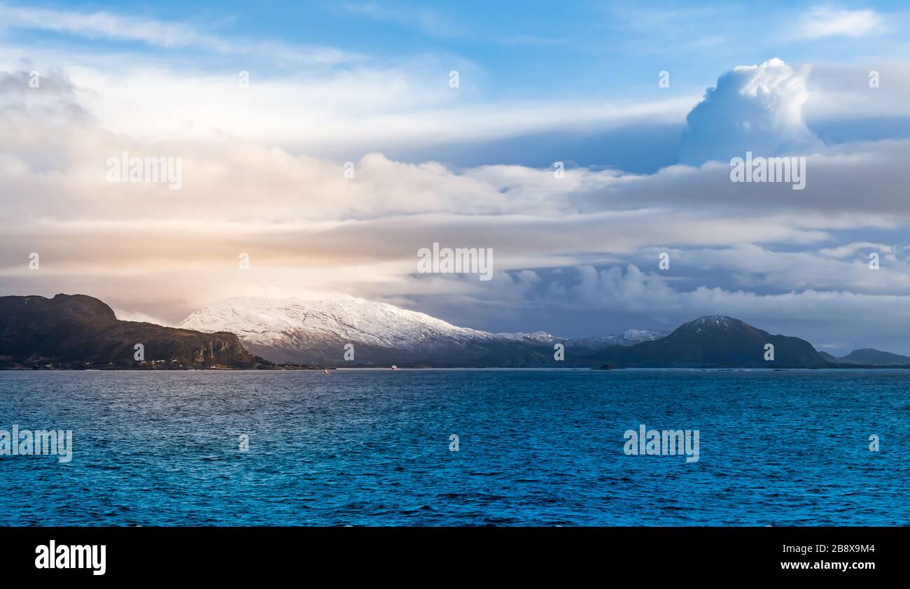 Atemberaubende panoramische Winter- und Meereslandschaft mit verschneiten Bergen und wunderschönen Wolken im Hintergrund. Norwegische See, Norwegen, Skandinavien. Stockfoto