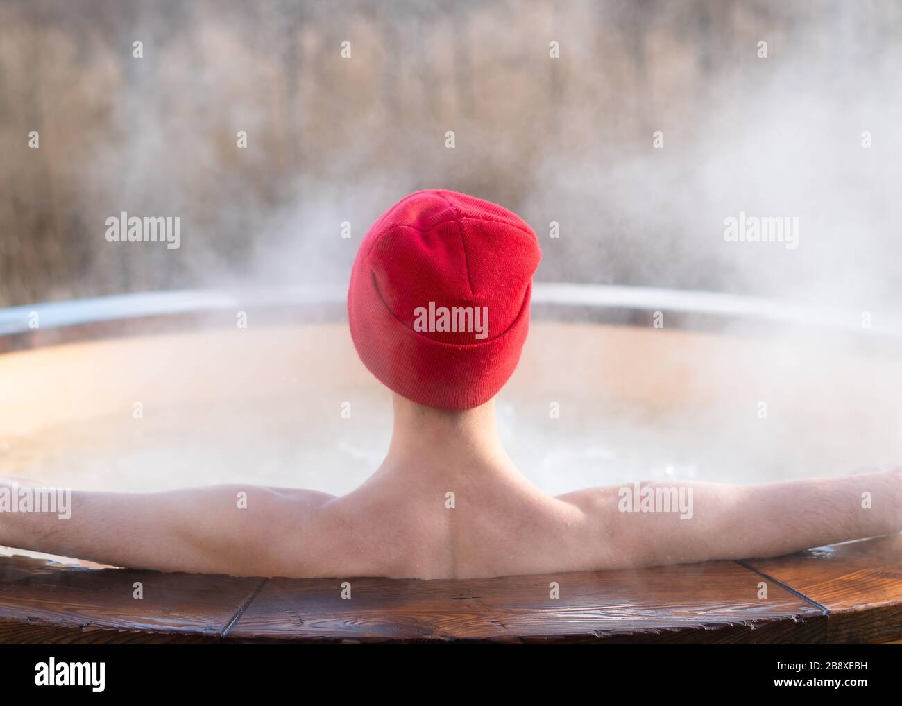 Junger Erwachsener, der draußen im Wannen-Whirlpool aus Holz entspannen und die Natur betrachten kann. Person, die an einem sonnigen Tag einen heißen Dampfpool genießen, private Spa-Behandlung Stockfoto