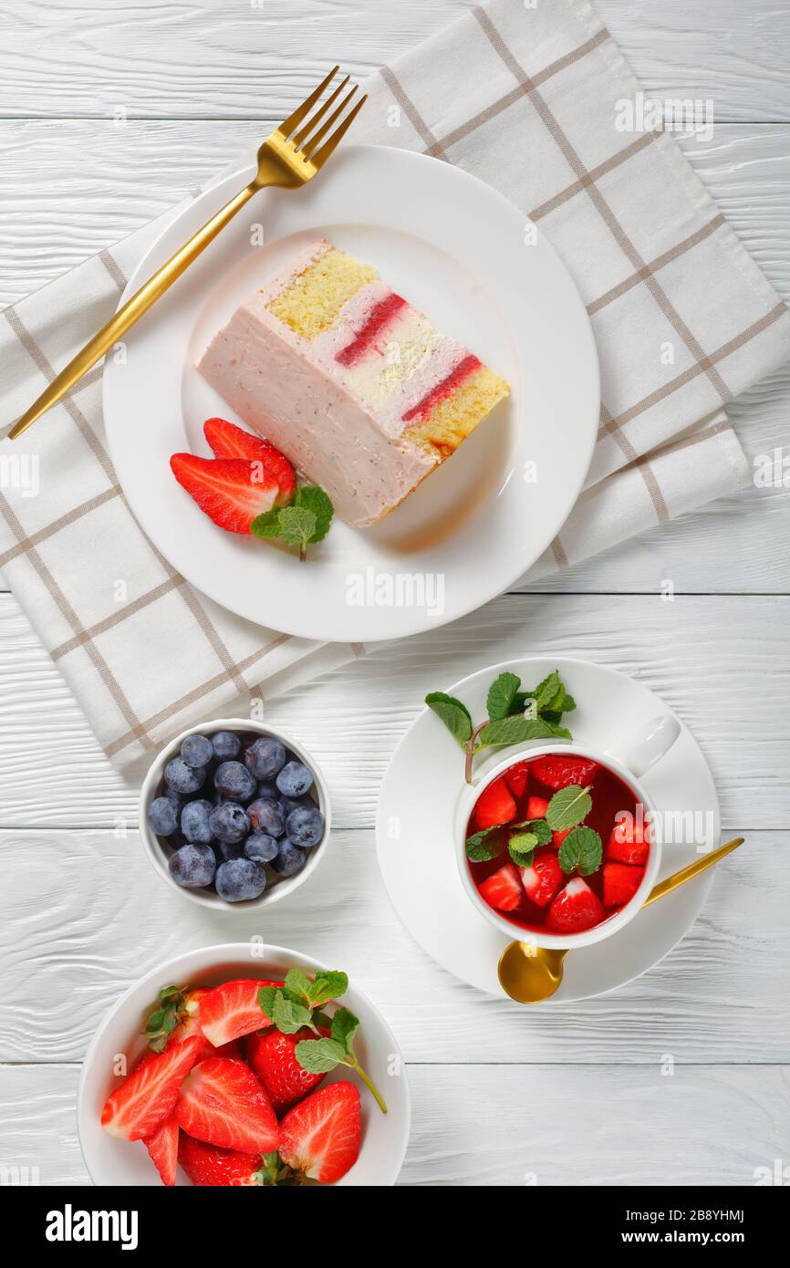 Eine Scheibe eines rosafarbenen Erdbeerchekakes, serviert mit frischen Beeren und Erdbeerlemonade in einer Tasse auf einem Holztisch, vertikale Ansicht von oben Stockfoto