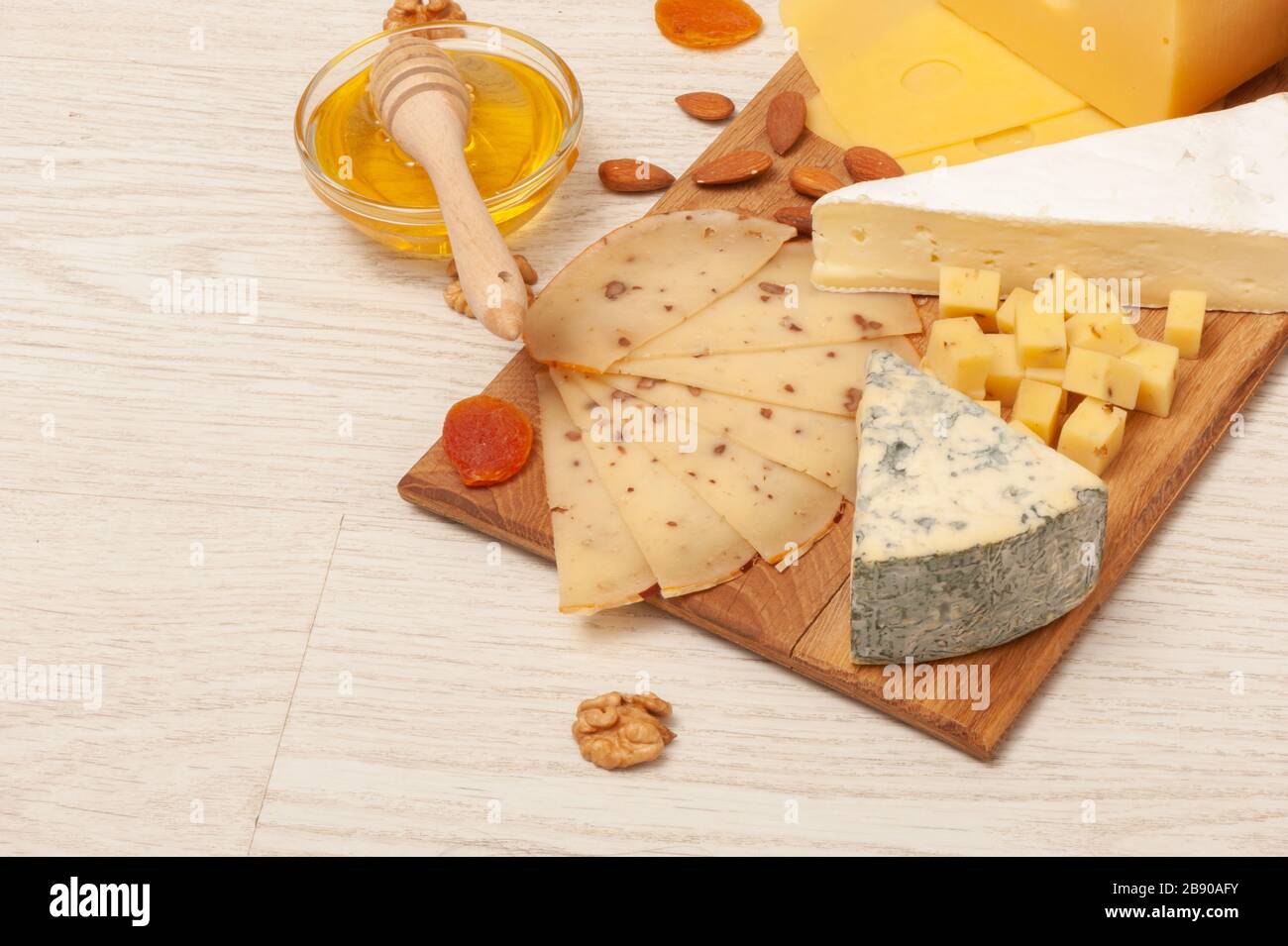 Verschiedene Käsesorten mit Nüssen und getrockneten Aprikosen und Honig auf einem Holzbrett. Draufsicht Stockfoto