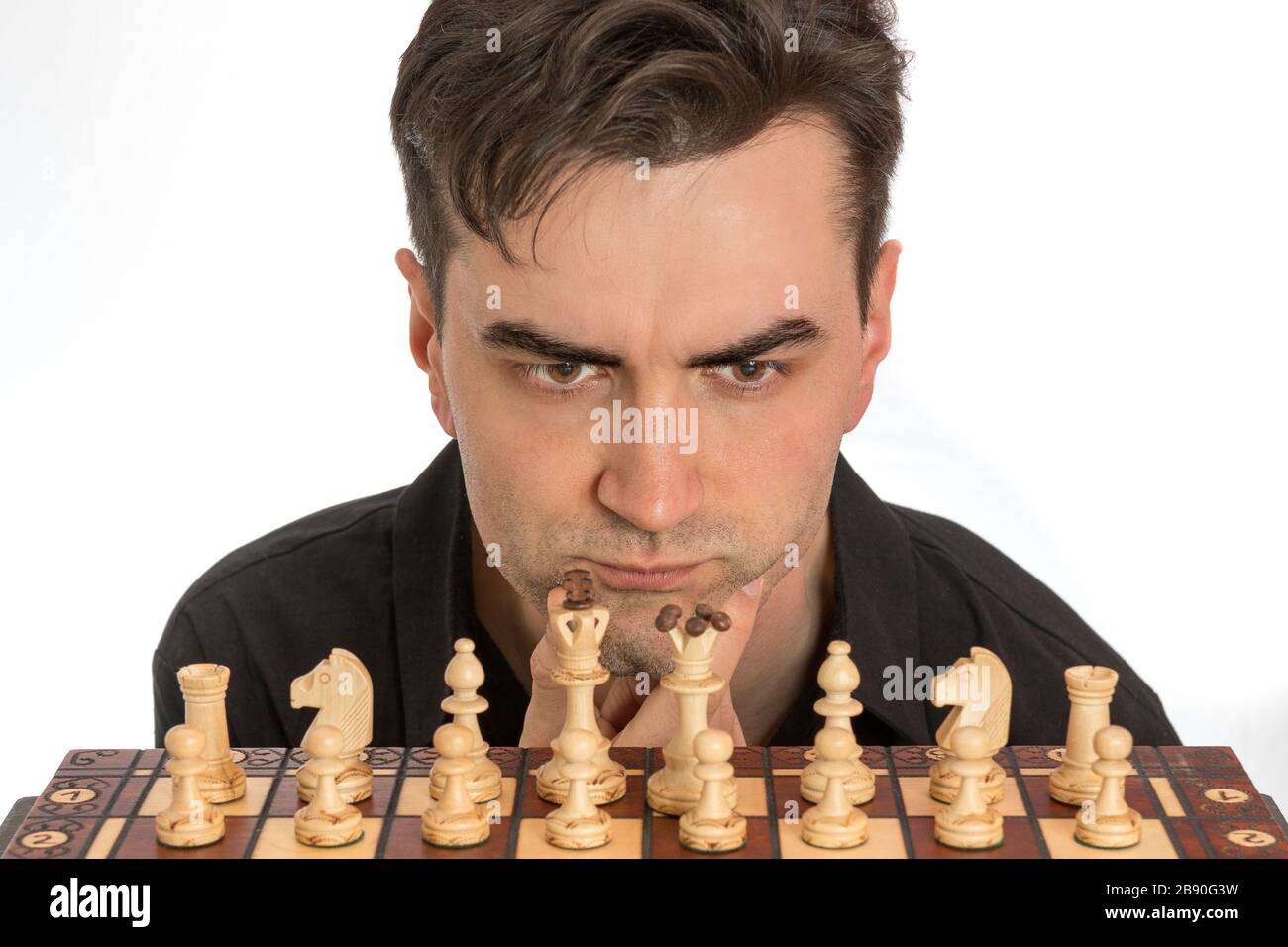 Männlicher Schachspieler erwägt seinen ersten Zug vor weißem Hintergrund. Lizenzfreies Foto. Stockfoto
