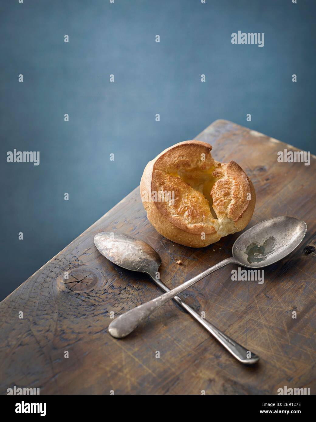 Single Yorkshire Pudding auf einem Holztisch aus Kiefernholz mit zwei verdisten Löffeln Stockfoto