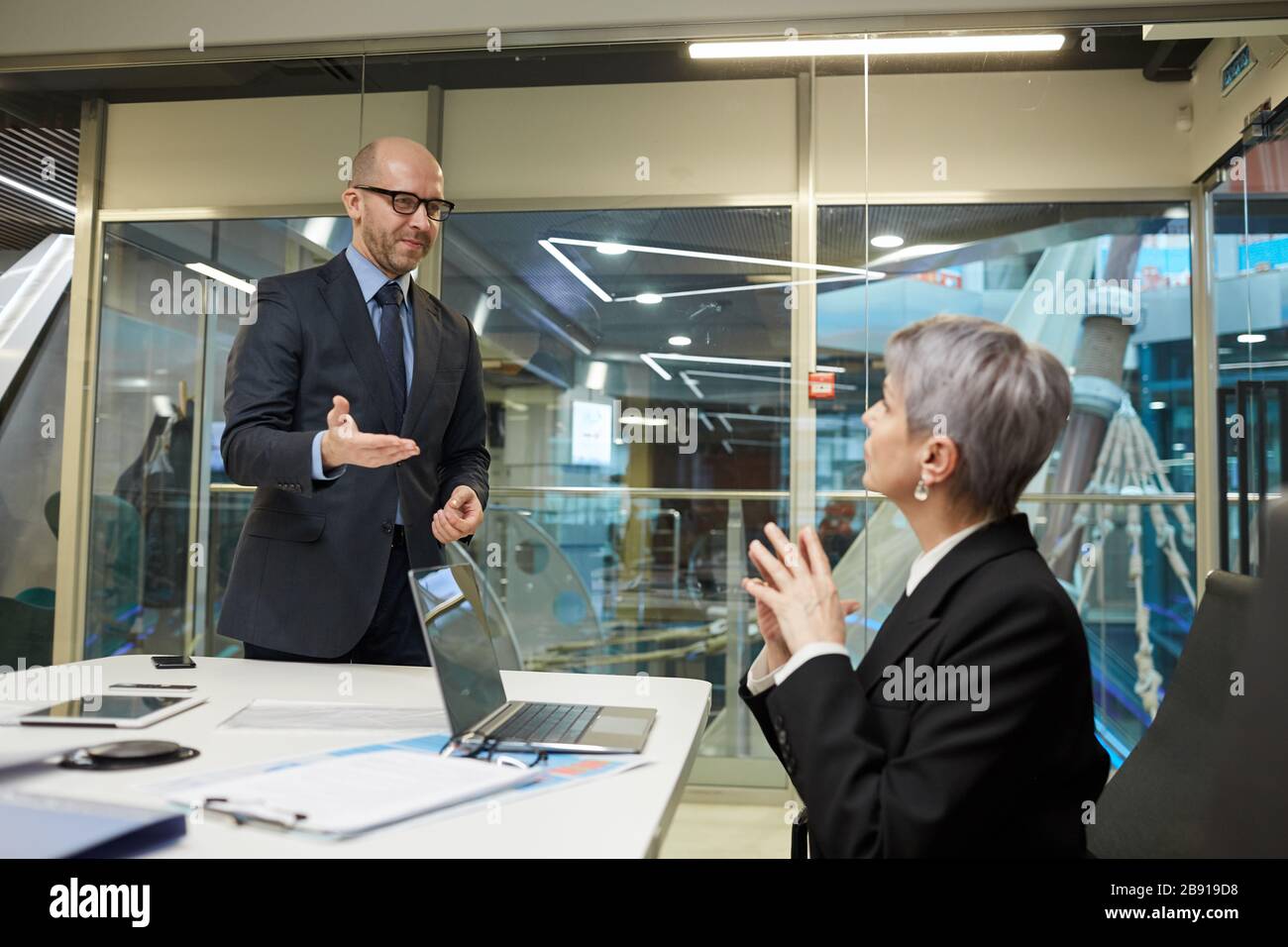 Portrait des lächelnden kahlen Geschäftsmannes, der die weibliche Kollegin im Besprechungsraum grüßt, Kopierer Stockfoto
