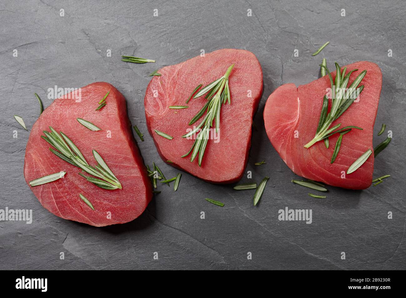 Rohes Thunfischsteak mit Rosmarin auf schwarzem Stein Stockfoto