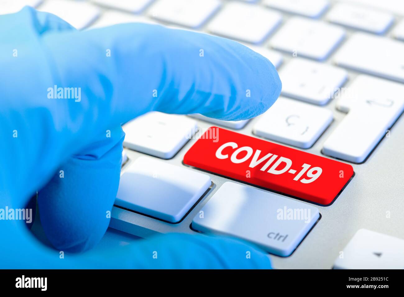 Hand mit Schutzhandschuh und Tastatur mit roter Taste und COVID-19-Meldung. Coronavirus Konzept Stockfoto