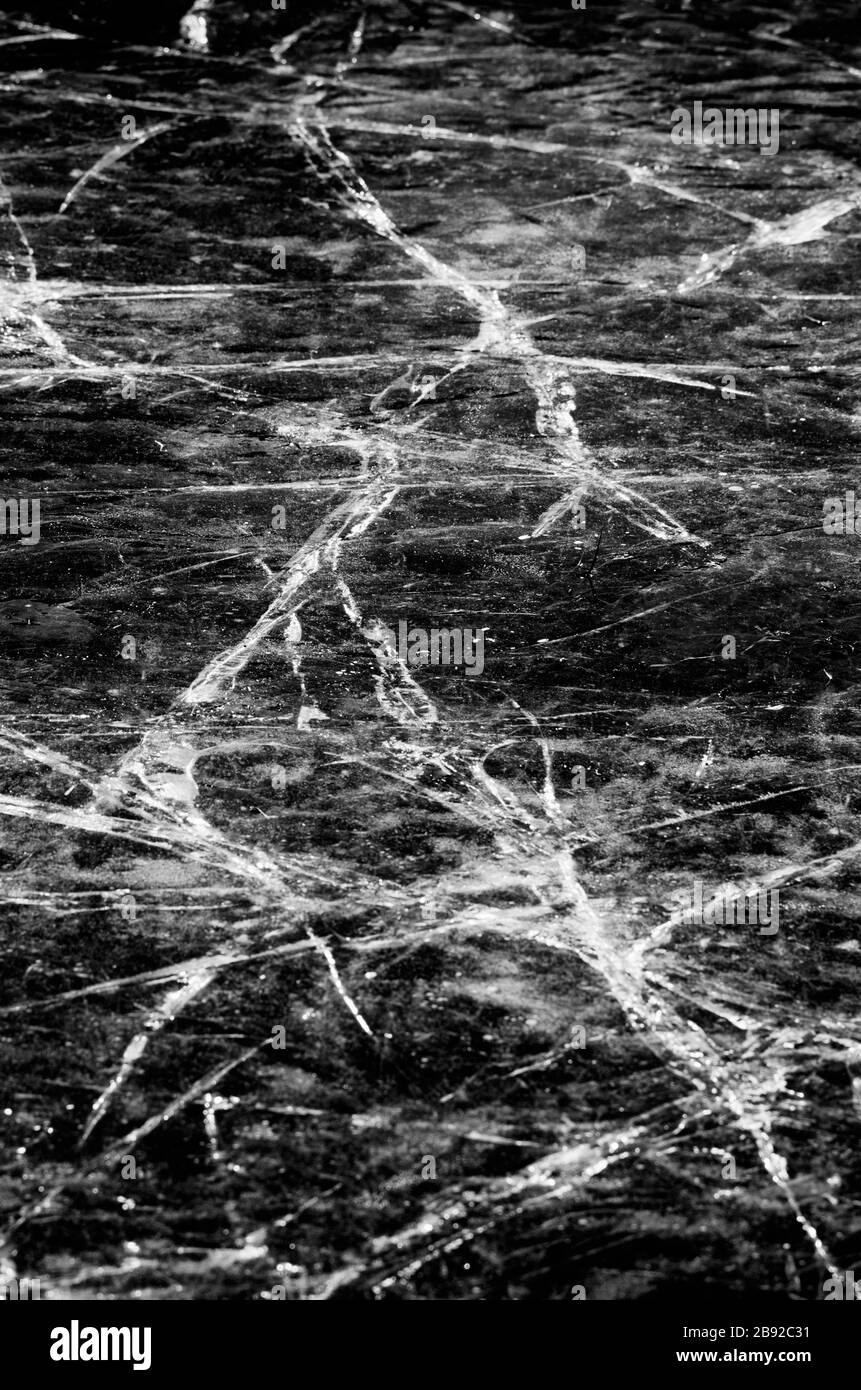 Natürliches Rissmuster auf der Eisdecke des Flusses in vertikaler Ausrichtung im Schwarz-Weiß-Stil Stockfoto