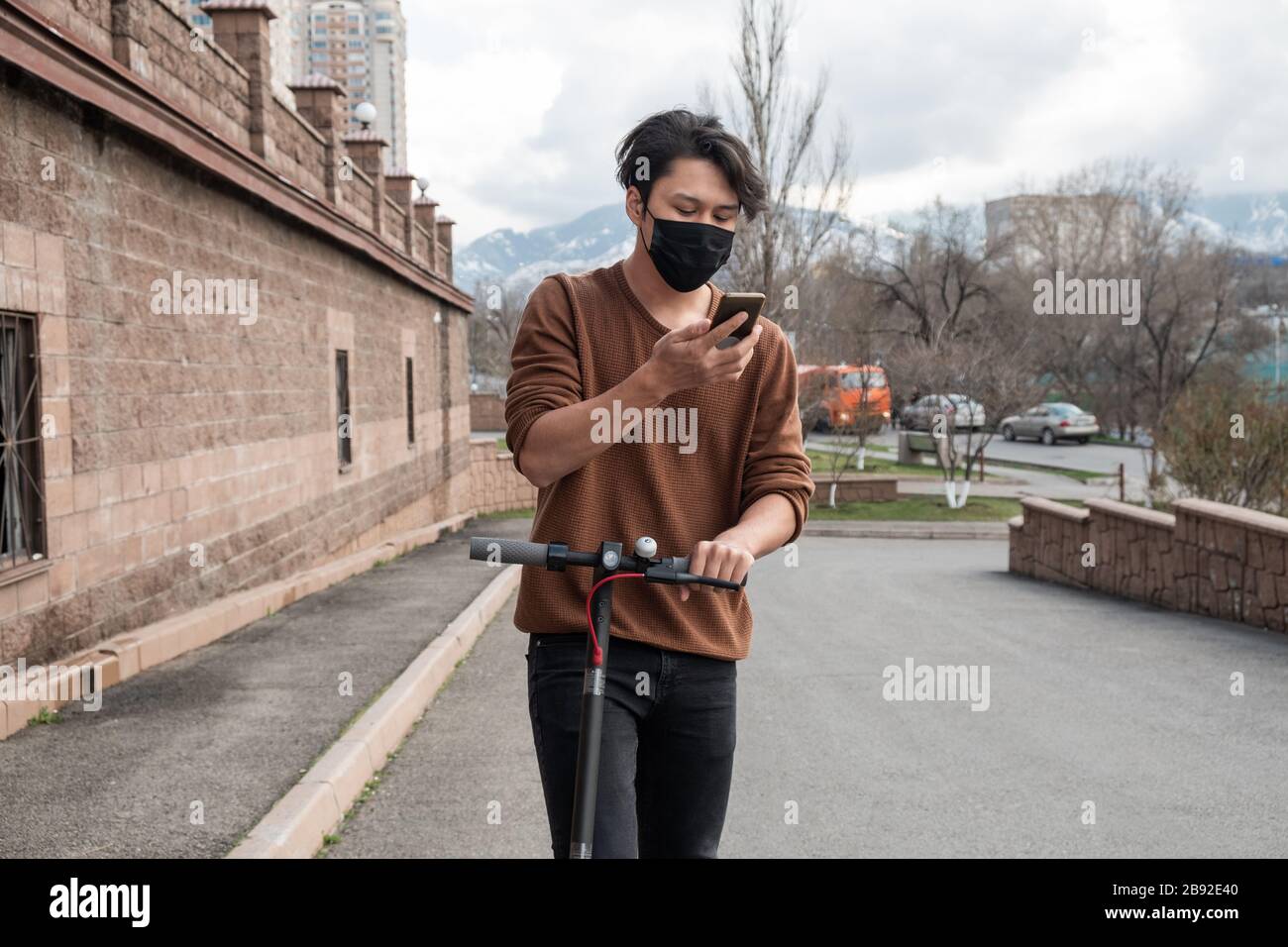 Junger Mann, der mit einem Roller unterwegs ist und mit dem Handy in der Stadt spricht Stockfoto