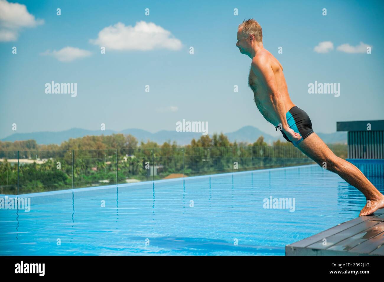 Unemotionaler lustiger Mann, der in den Swimmingpool fällt. Sommerurlaub Stockfoto