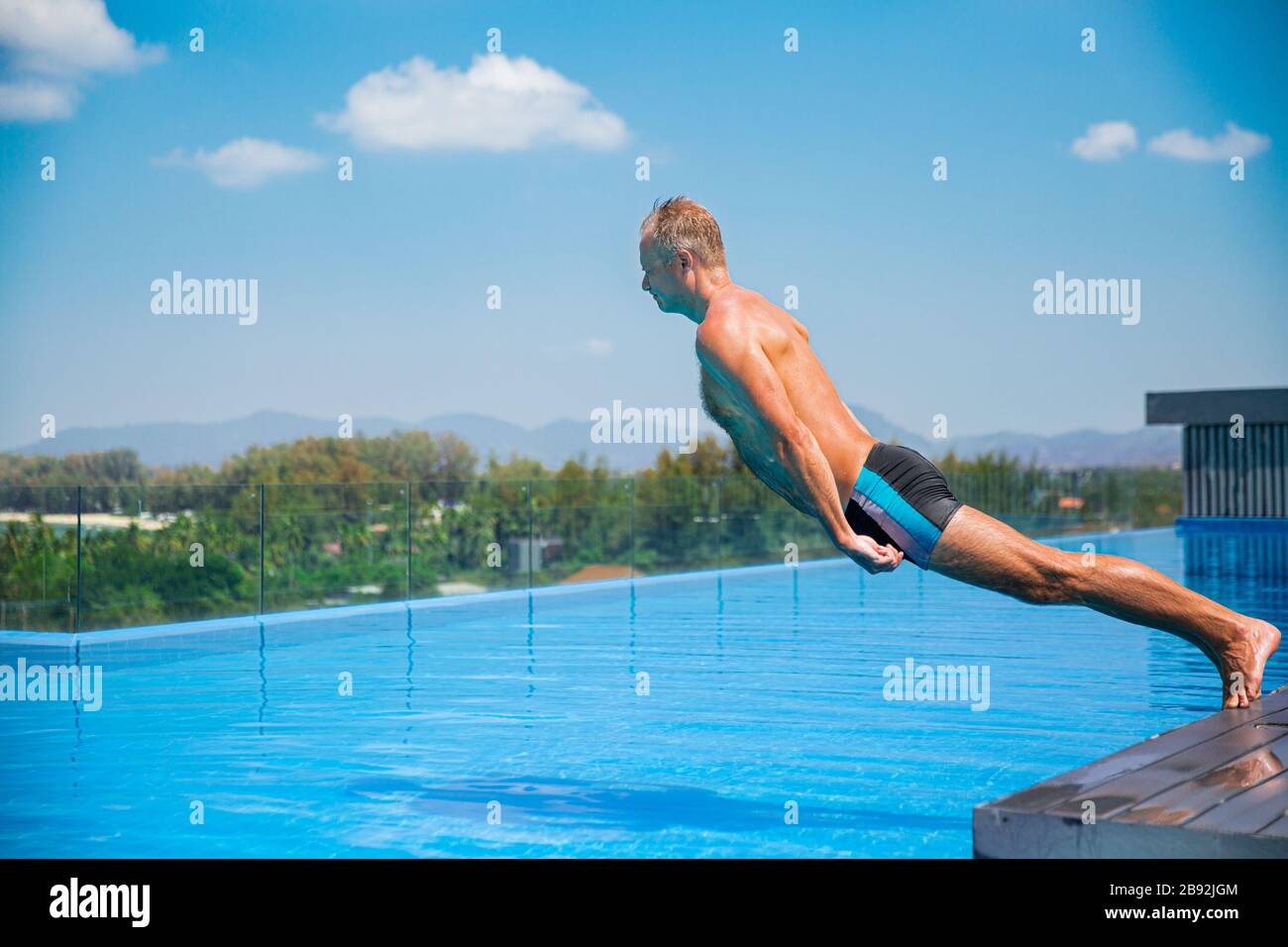 Unemotionaler lustiger Mann, der in den Swimmingpool fällt. Sommerurlaub Stockfoto