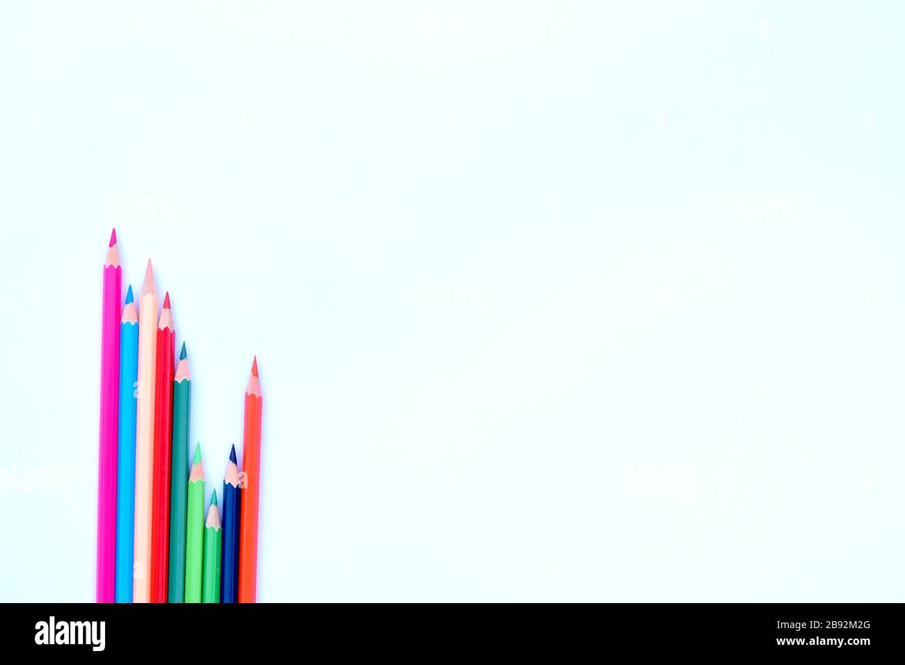 Acht verschiedenfarbige Bleistiftkrebse, die in einer winkelten, gesparten Reihe an einer Ecke mit weißem Hintergrund versammelt waren Stockfoto