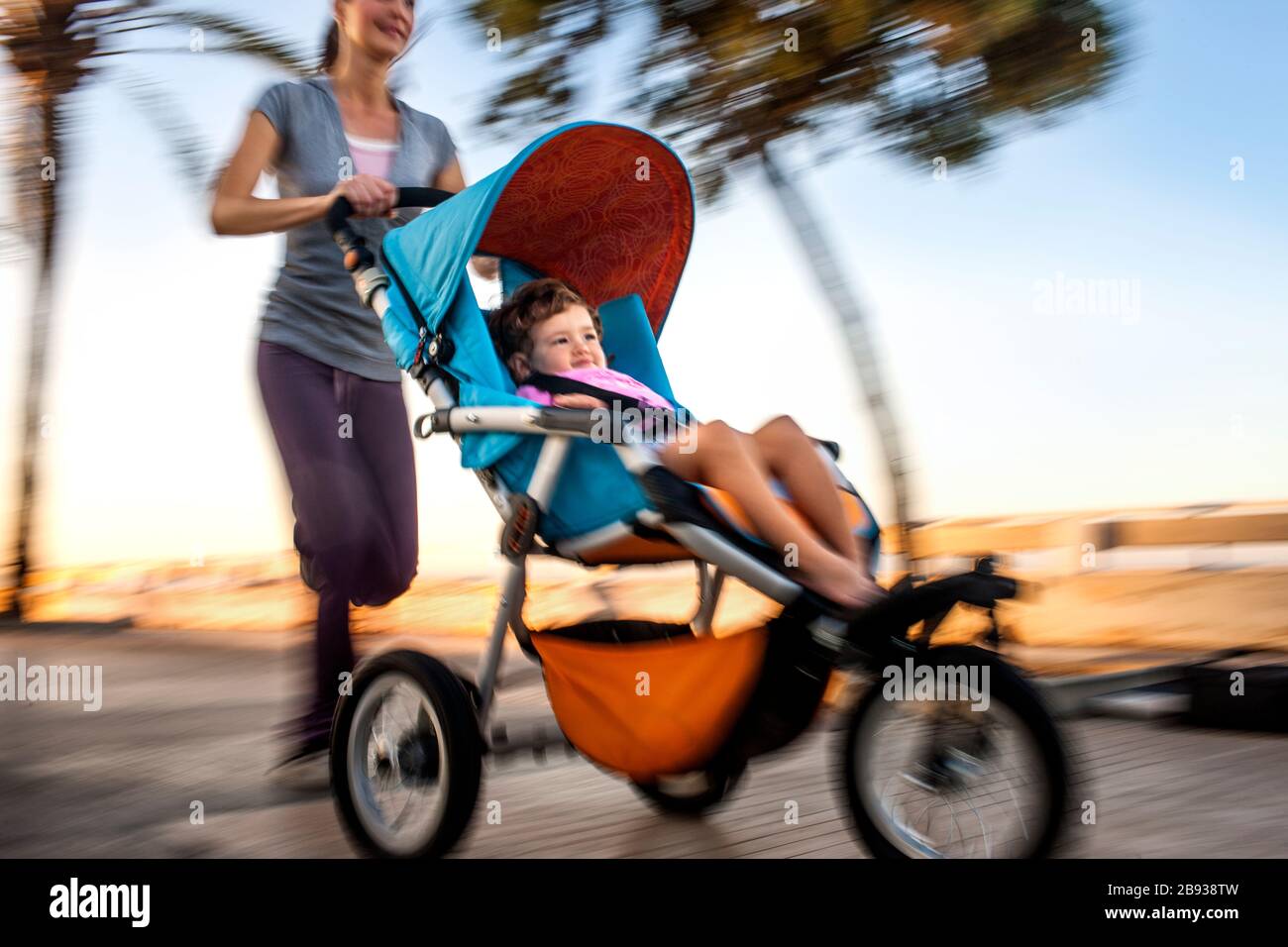 Frau joggt, während sie ihre Tochter in einen Kinderwagen schiebt. Stockfoto