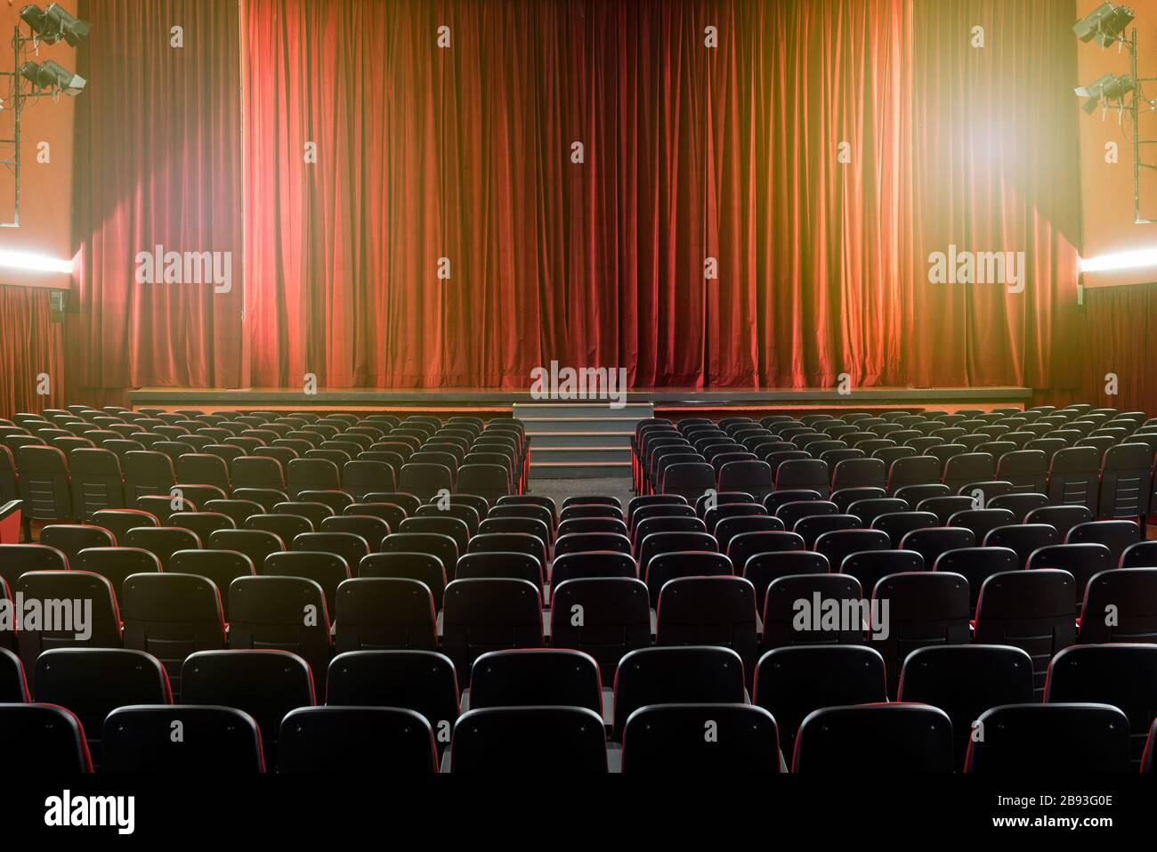 Großer beleuchteter Theatersaal mit leeren Sitzplätzen von hinten in Richtung Bühne mit geschlossenem roten Vorhang in einem darstellenden Kunstkino Stockfoto