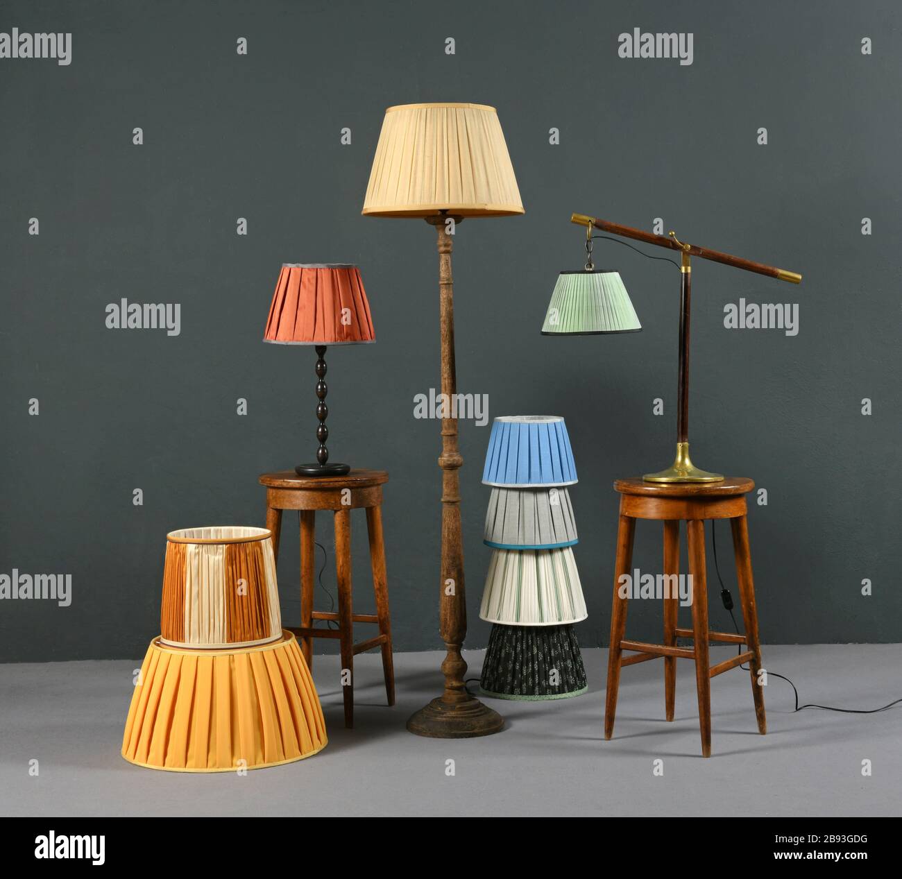 Eine Sammlung farbenfroher, flierter Lampenschirme aus Vintage-Farben, die mit einer Standleuchte auf dem Boden, einer abgewinkelten Hängelampe und einer kleinen Tischleuchte in einem Grauton kombiniert werden Stockfoto