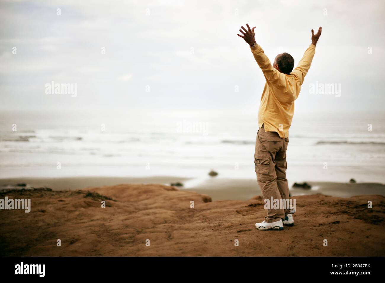 Mann steht auf dem Felsen auf dem Meer mit offenen Armen Stockfoto