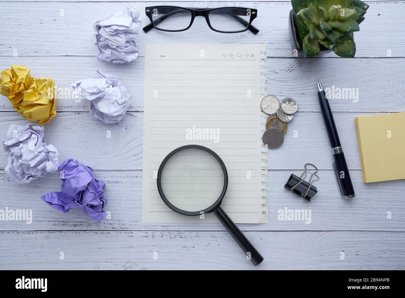 Bunte zerknitterte Papierkugel, Stift und Lupe auf dem Tisch Stockfoto
