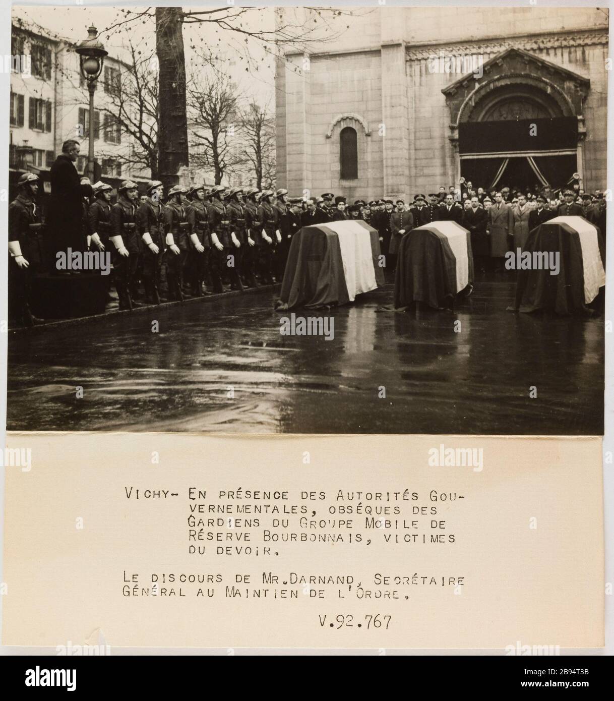 Fotografie-Propaganda-Erinnerung vor den Särgen bei der Beerdigung der Wächter der mobilen Gruppe bourdonnais Reserve Vichy Trampus. "Photographie propagande: Recueillement devant les cercueils lors des obsèques des gardiens du groupe mobile de Réserve bourdonnais, Vichy". VICHY- EN PRESENCE DES AUTORITES GOU- / VERNEMENTALES , OBSEQUES DES / GARDIENS DU GROUPE MOBILE DE / RESERVE BOURDONNAIS, VICTIMES / DU DEVOIR. / LE DISCOURS DE MR. DARNAND, SECRETAIRE / GENERAL AU MAINTIEN DE L'ORDRE. / V.92.767. Tirage au gélatino-bromure d'argent. Légende dactylographiée à l'encre noire. De Stockfoto