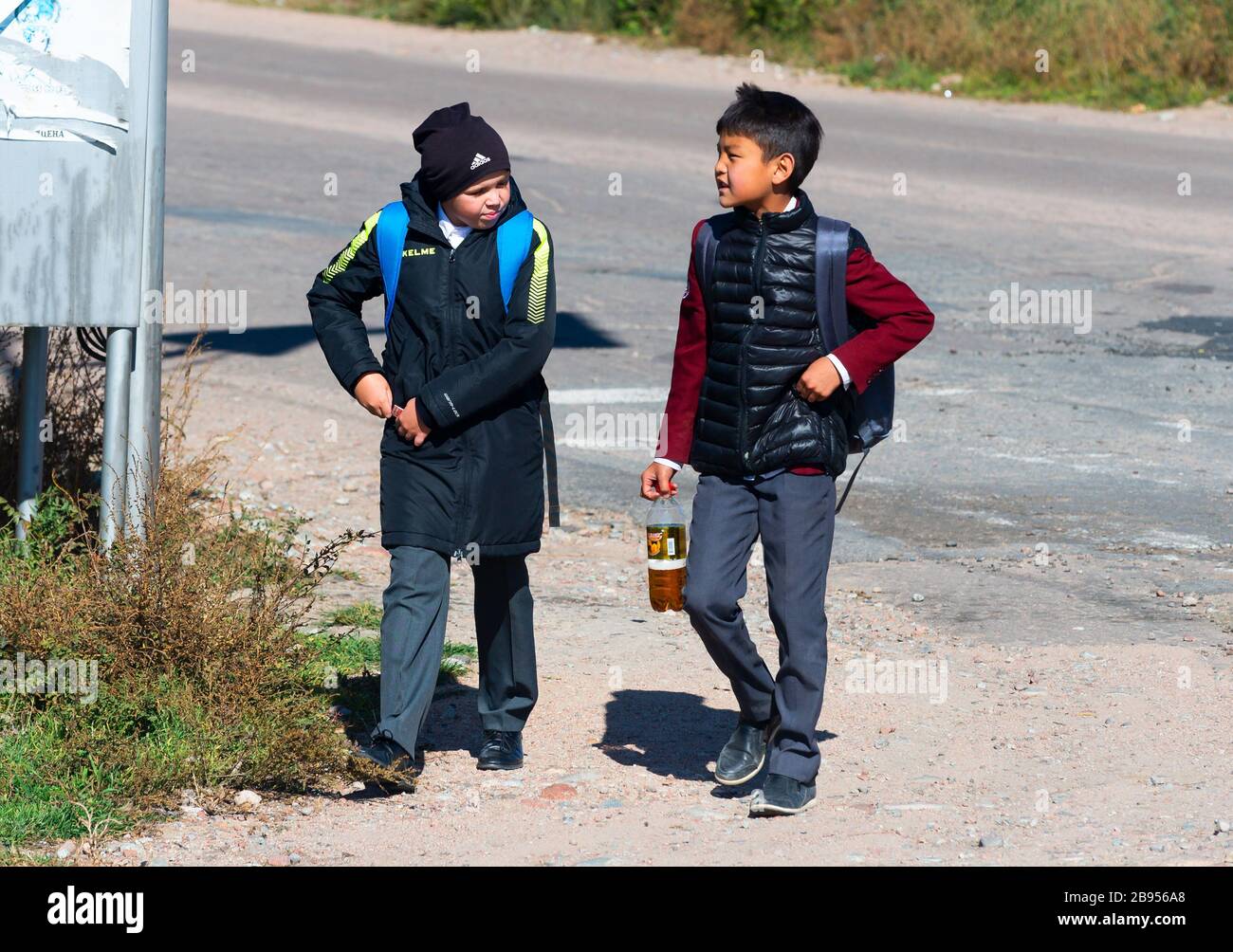 Zwei junge kirgisische Jungen, die von der Schule gehen, tragen kalte Kleidung und Rucksack. Kinder reden im ländlichen Kirgisistan in der Nähe von Karakol in Issyk Kul Region. Stockfoto