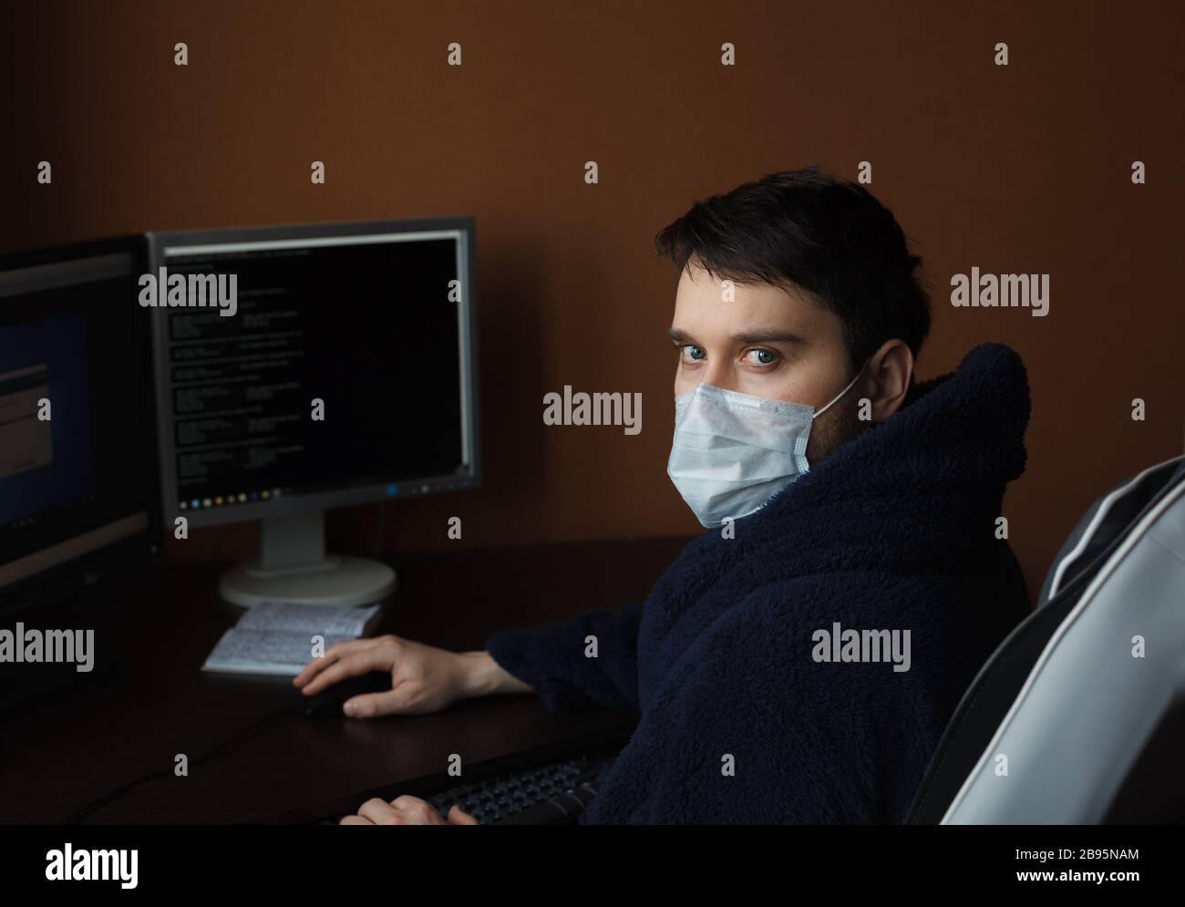 Mann arbeitet während der Quarantäne von zuhause aus. Mann in der Medizin Maske und Gown. Coronavirus (Covid-19)-Ausbruch Stockfoto