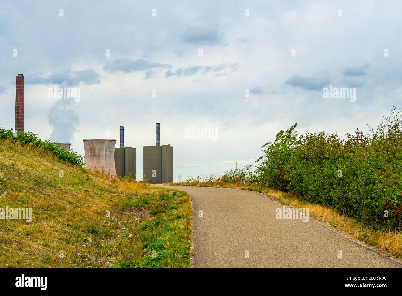 Blick über Wiesen, Wege und Büsche zu einem Kraftwerk mit dampfendem Kühlturm am Horizont Stockfoto