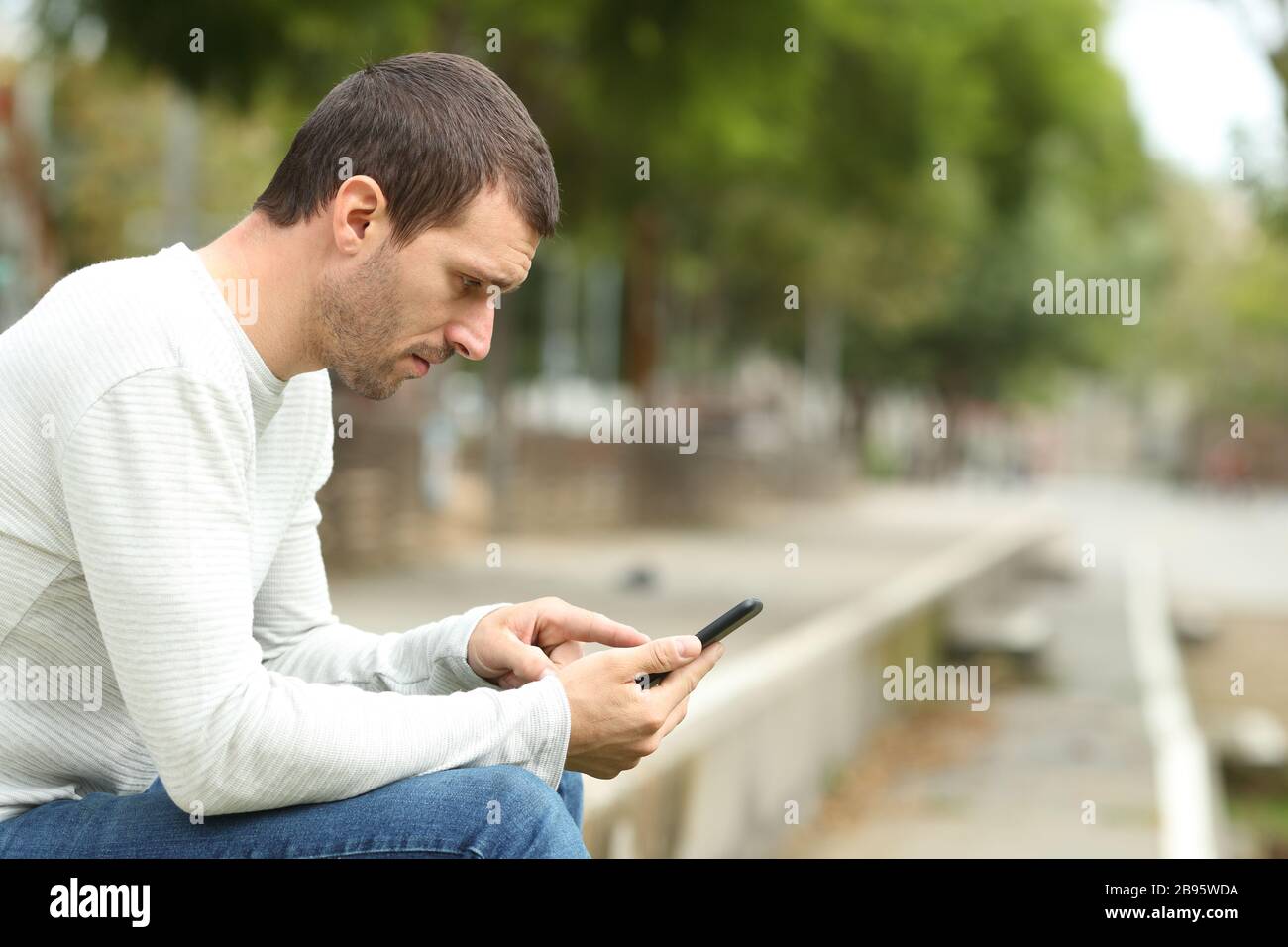 Seitenansicht eines ernsthaften erwachsenen Mannes mit Smartphone allein in einem Park Stockfoto