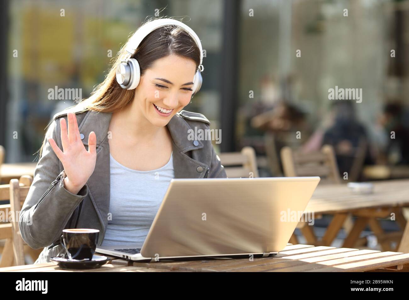 Glückliche Frau, die auf einem Laptop ein schnurloses Headset-Videoband trägt und auf einer Café-Terrasse sitzt Stockfoto