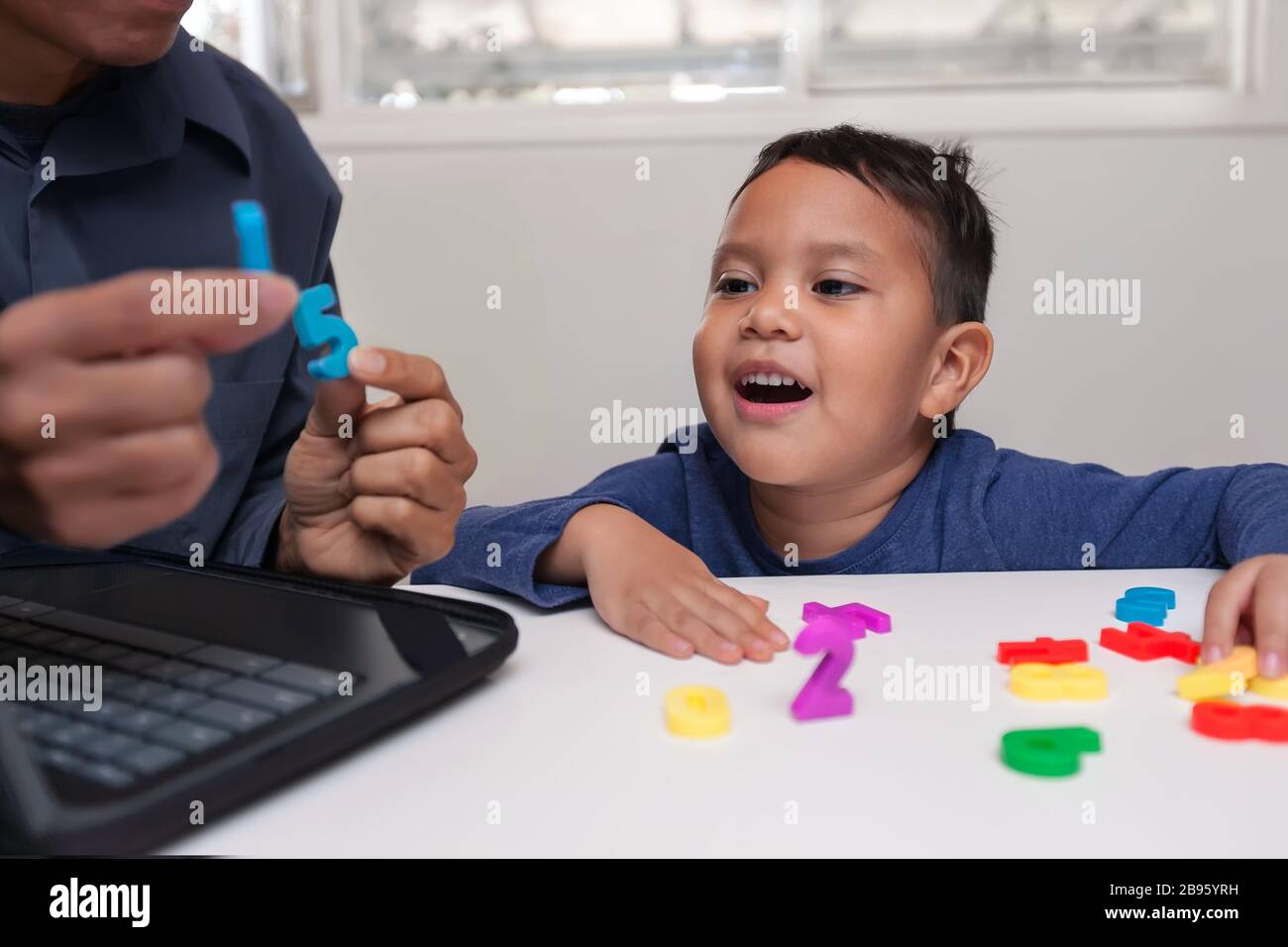Hausstudie mit Tutor, der einem jungen Jungen beigebracht hat, wie mit Hilfe von Zahlenmanipulativen gezählt werden kann, und das Kind, das die richtige Antwort spricht. Stockfoto
