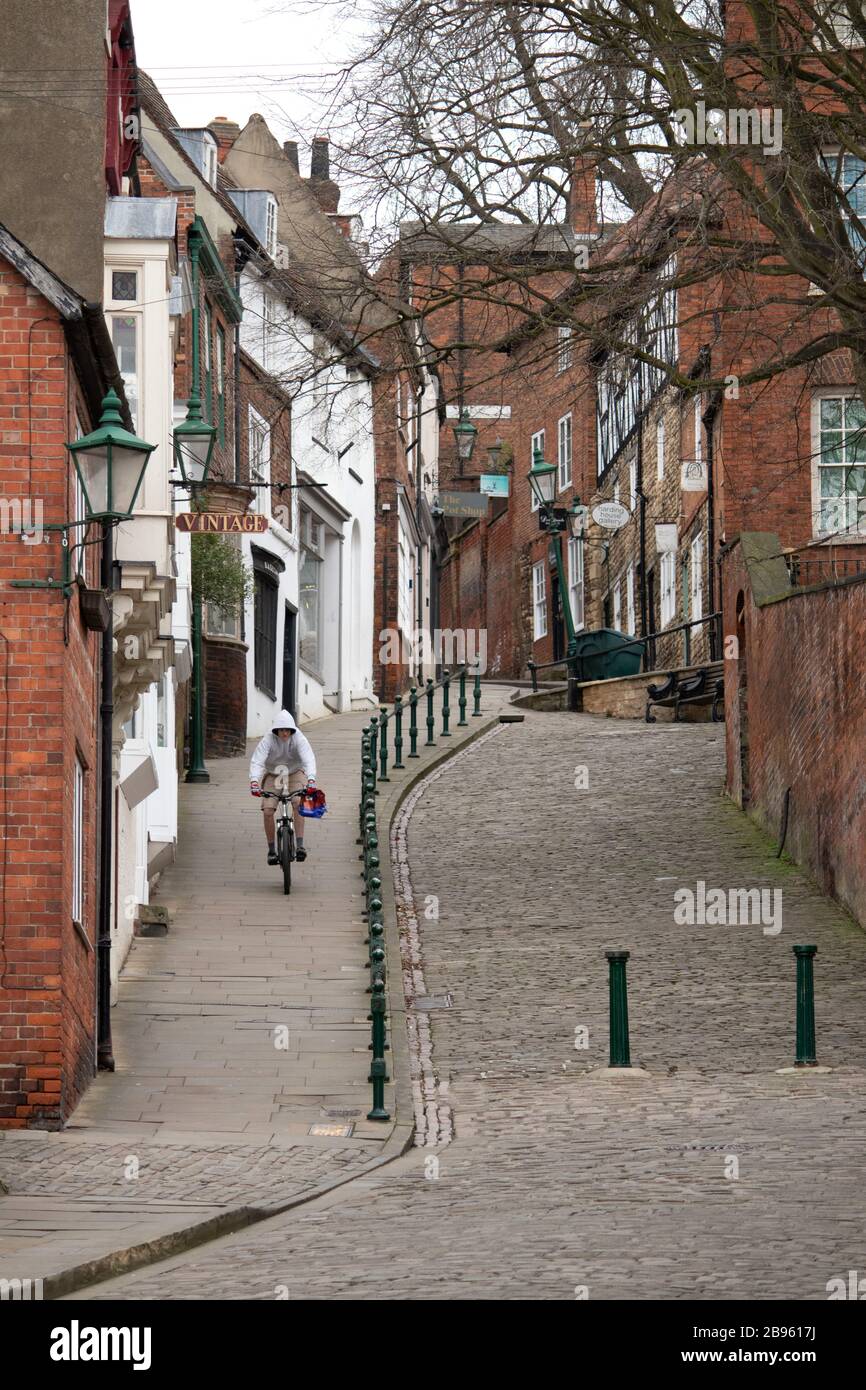 Ein einsamer Radfahrer, der auf dem Steep Hill, Lincoln, radelt. Steep Hill ist einer der meistbesuchten Orte in der Stadt Lincoln in der englischen Grafschaft Lincoln. Steep Hill verbindet Lincoln bergauf mit dem Stadtzentrum und dem Einkaufszentrum, die sich auf der Ebene befinden. Sie war früher als Ermine Street bekannt und wird derzeit vom County Council von Lincoln County unterhalten. Stockfoto