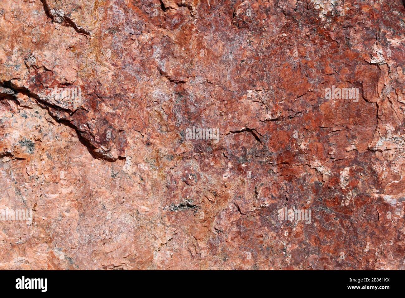 Nahaufnahme eines großen massiven Steins in Rot-, Orange- und Schwarztönen. In diesem Foto sehen Sie die rustikale Struktur der unebenen Oberfläche des Felsens im Detail. Stockfoto