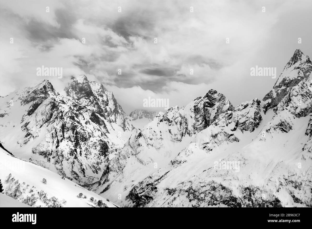 Graue hohe Berggipfel, die im Winter mit Eis und Wolken bedeckt sind. Kaukasusgebirge, Region Dombucht. Schwarz-weiß getonte Landschaft. Stockfoto