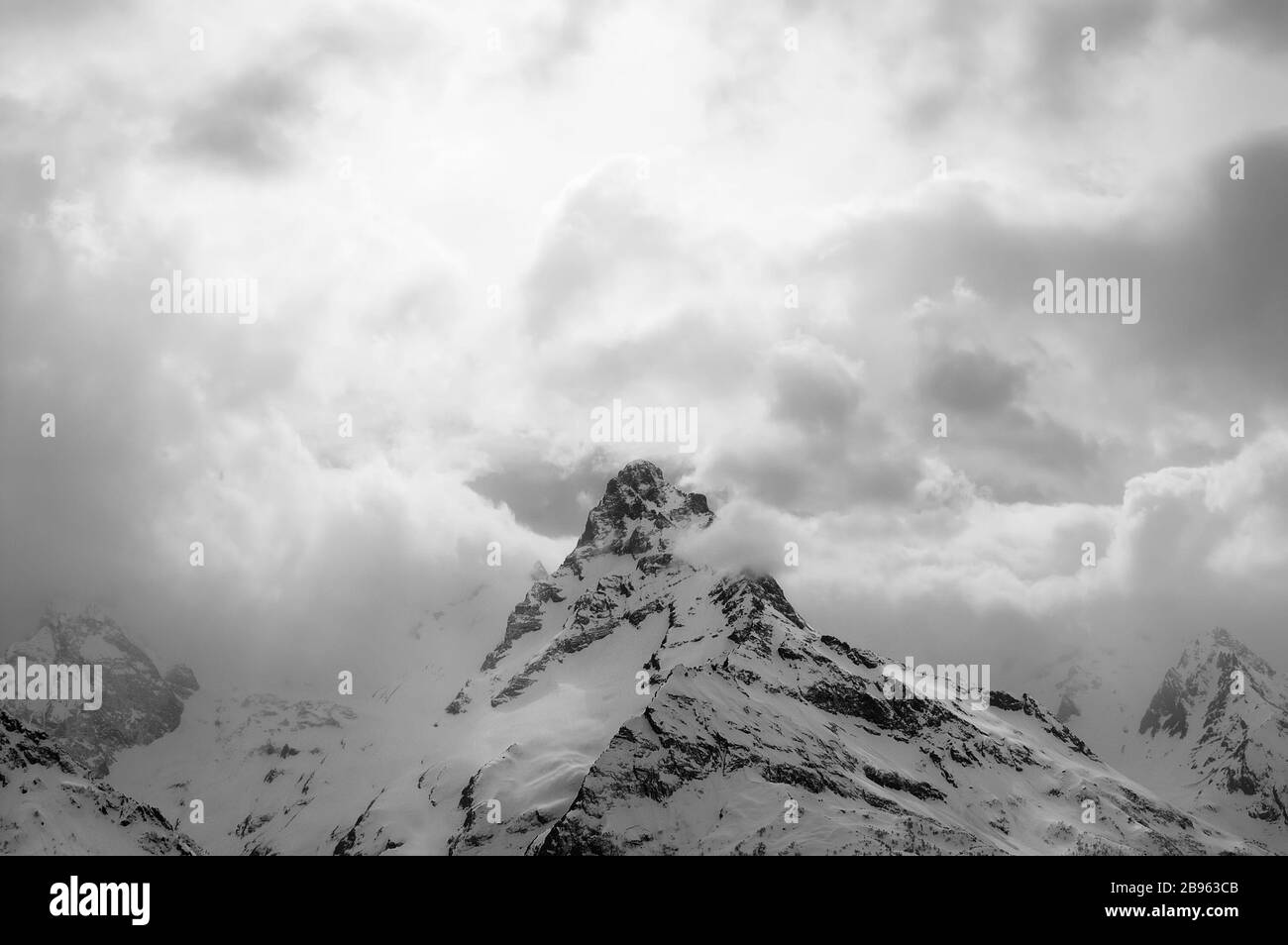 Schwarz-weiß hohe Berggipfel mit Eis und Himmel und Wolken am Winterabend. Kaukasusgebirge, Region Dombucht, Berg Belalakaya. Stockfoto