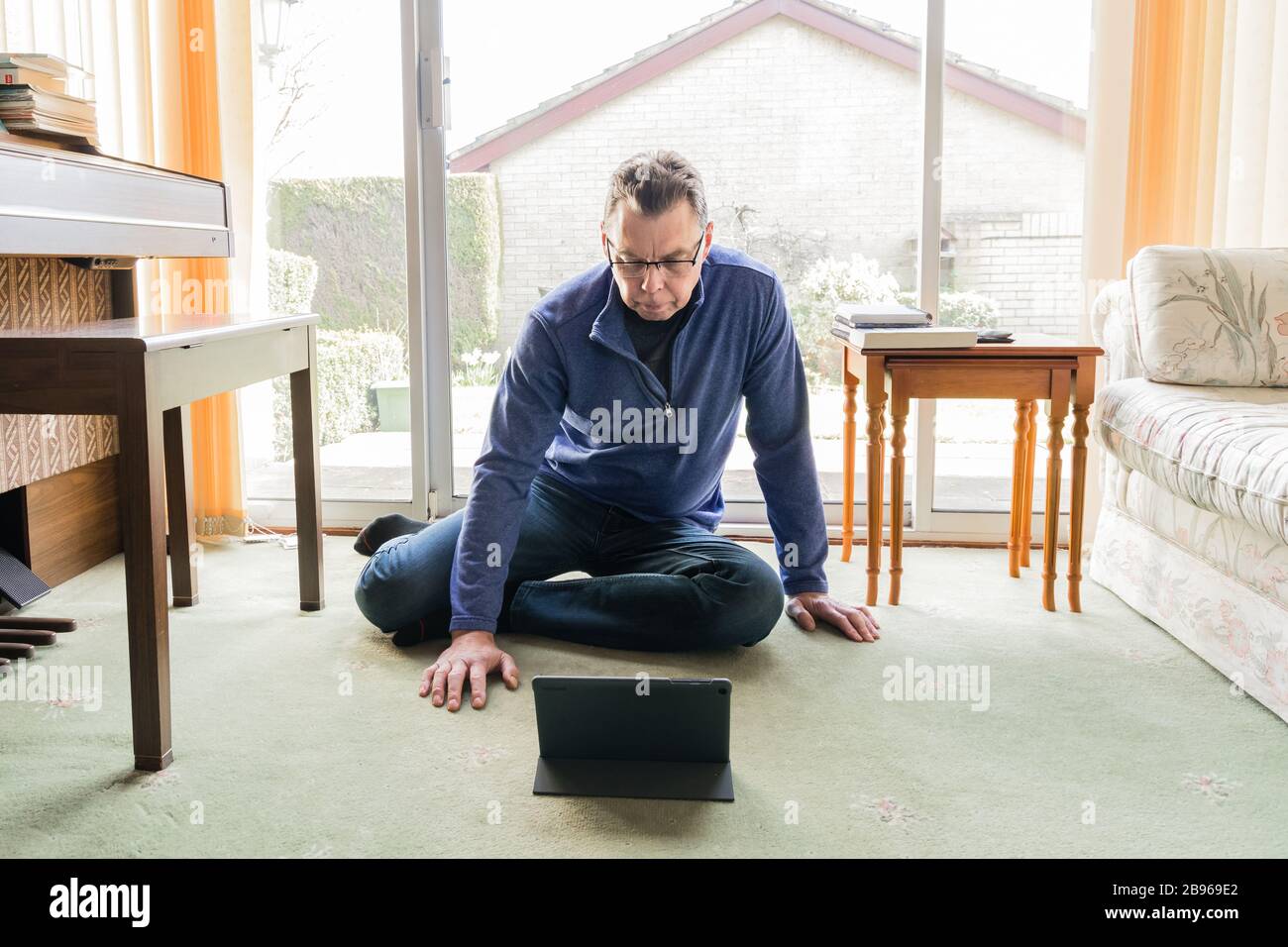 50 etwas männlich in Coronavirus Selbstisolierung zu Hause, sitzend vor dem Fenster im Wohnzimmer, mit Blick auf Tablet-Computer-Pad Stockfoto