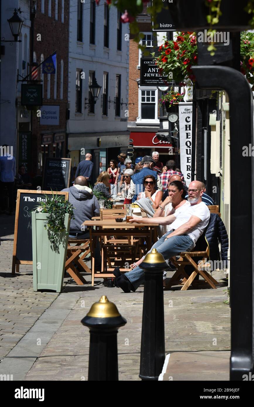 Leute, die in der Sommersonne an Tischen außerhalb von Bars sitzen, auf einer gepflasterten Straße namens Butcher Row in Shrewsbury, Shropshire UK Stockfoto