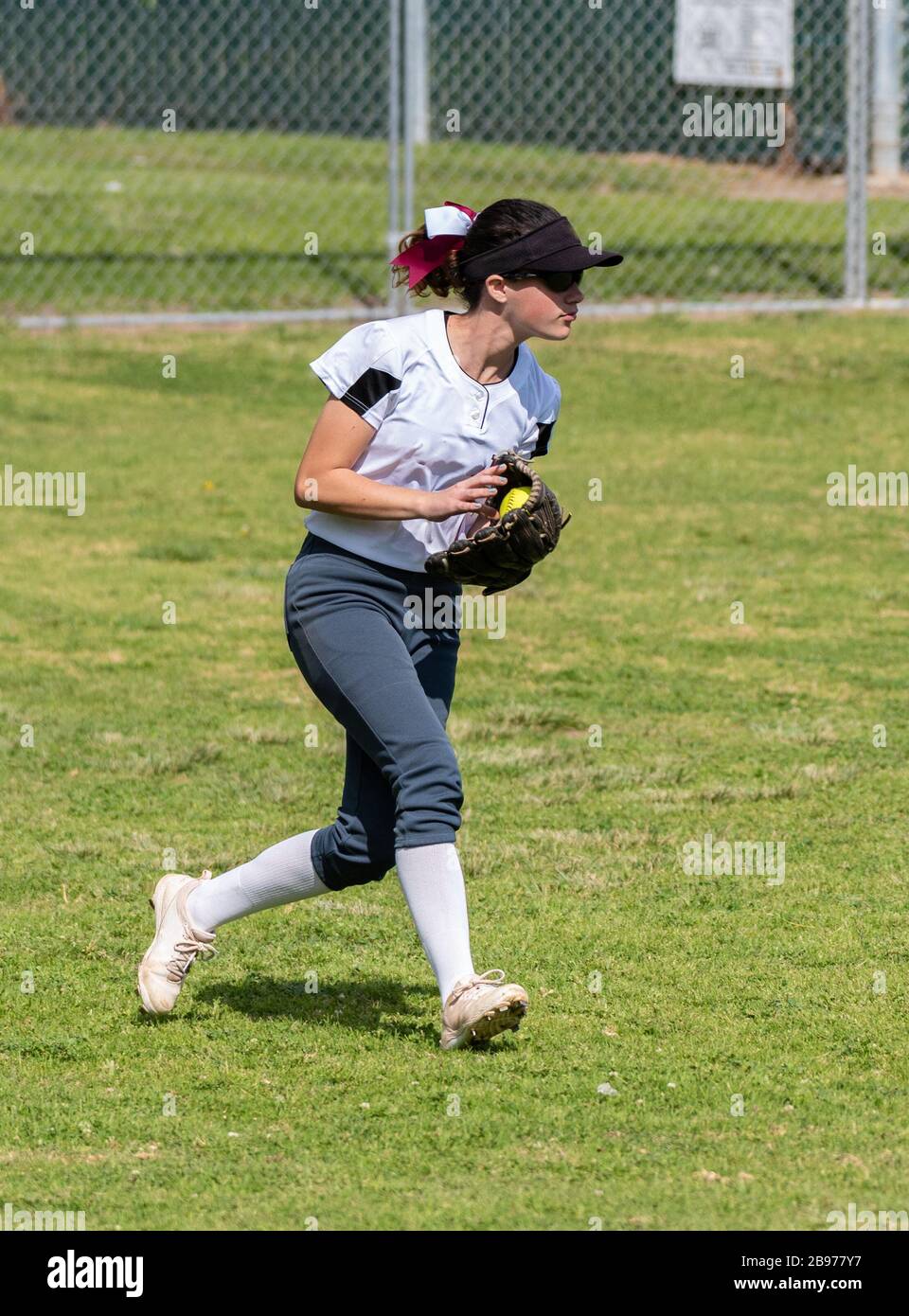 Softballausleger mit schnellem Spielfeld und Sonnenbrille, die im Außenfeld auf dem Rasen einen Ball im Spiel abhandhabt. Stockfoto