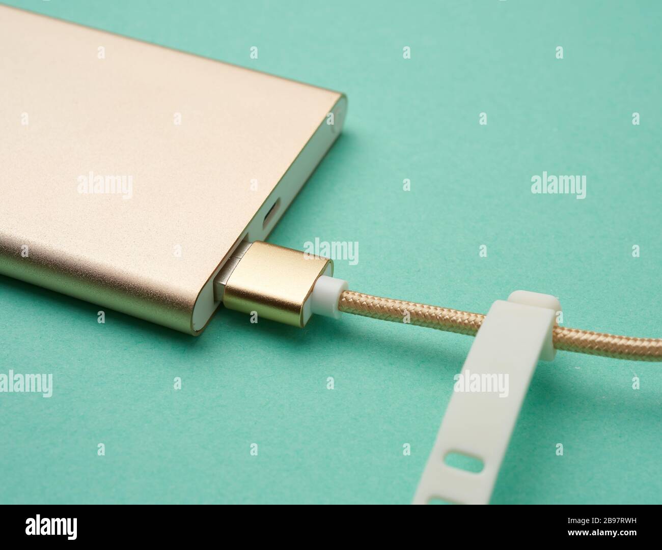 goldene Powerbank und Kabel mit USB-Anschluss zum Aufladen mobiler Geräte auf grünem Hintergrund, Draufsicht Stockfoto