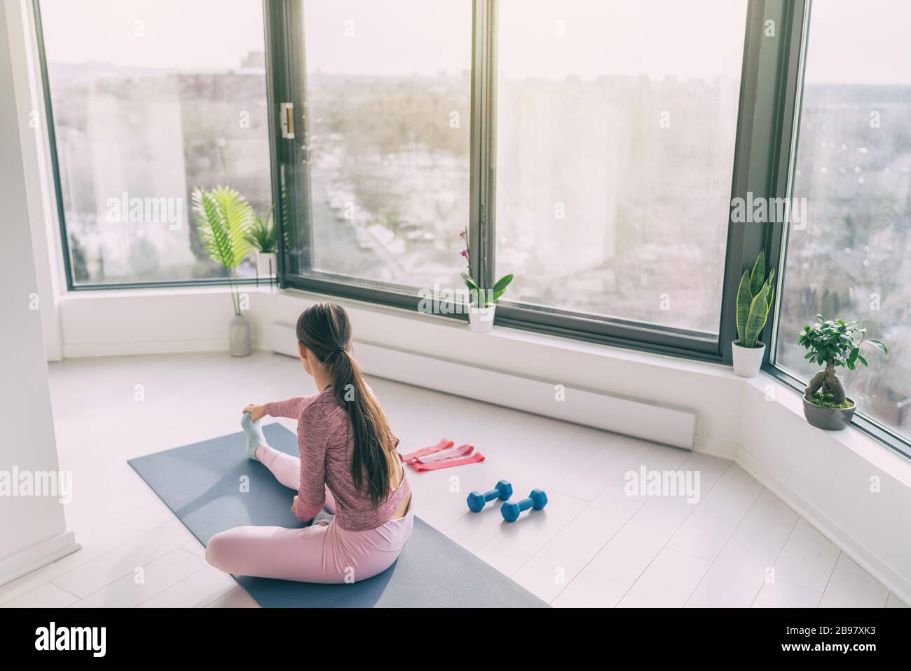 Home Fitness Yoga Workout Frau Training zu Hause Stretching Beine Aufwärmen Training. Fit Mädchen arbeiten in der Morgensonne im Wohnzimmer von Stockfoto