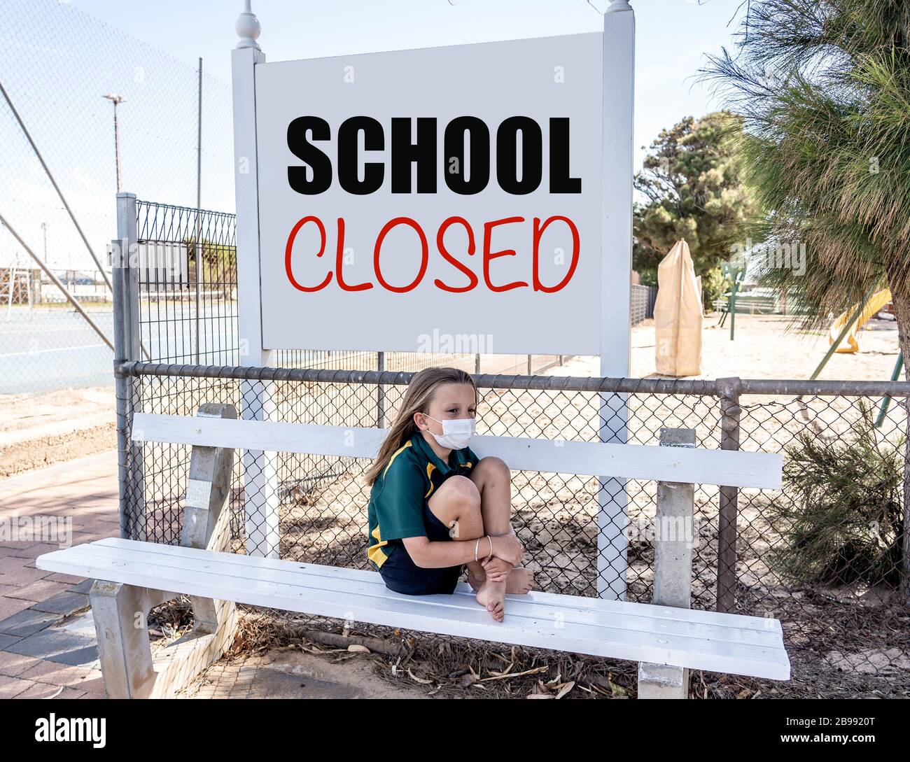 Covid-19 Ausbruchschulen geschlossen. Trauriges und gelangweiltes Schulmädchen Kind mit Gesichtsmaske, das sich depressiv und einsam vor ihrer geschlossenen Schule fühlt. Einschränkungen a Stockfoto