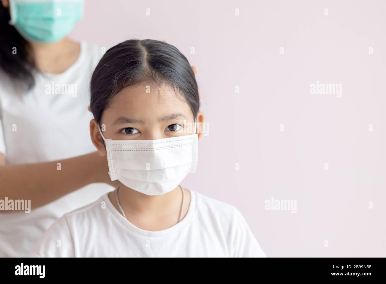 Asiatisches kleines Mädchen, das eine medizinische Schutzmaske trägt. Prävention der Ausbreitung von Influenza, Coronavirus oder COVID-19 und Smog Krankheit. Mutter zärnte Haare Stockfoto