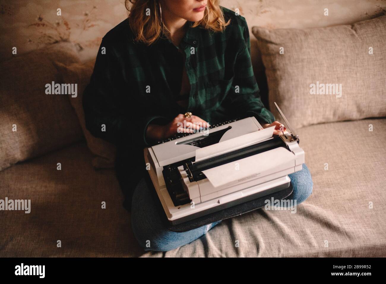 Junge Schriftstellerin, die Schreibmaschine verwendet, während sie zu Hause auf dem Sofa sitzt Stockfoto