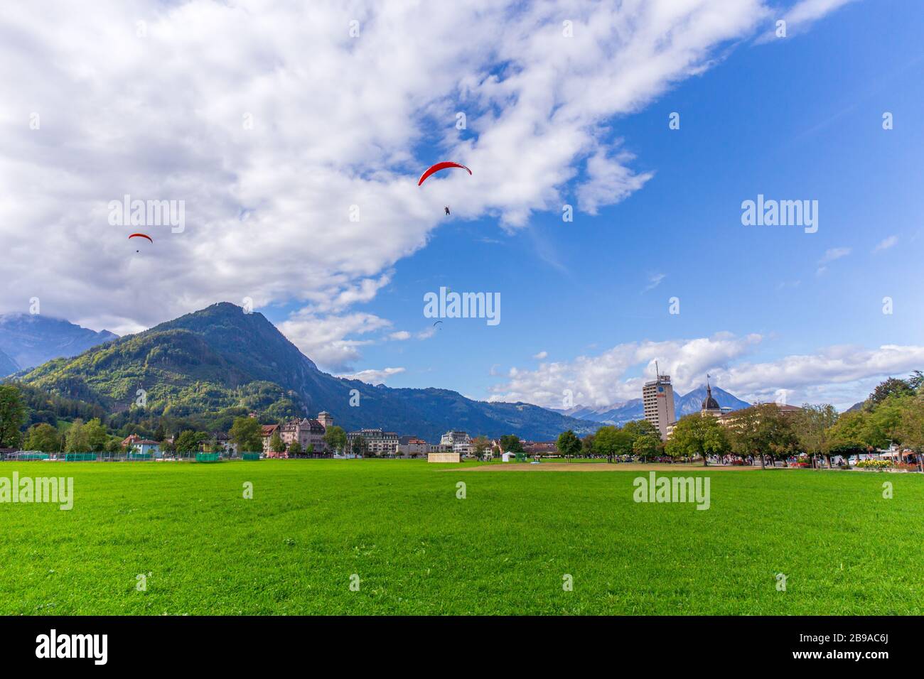 Interlaken, Schweiz - 28.09.2019 - landschaftlich grünes Feld mit Gleitschirm über Bergkette und blauem Himmel. Interlaken liegt zwischen dem Stockfoto