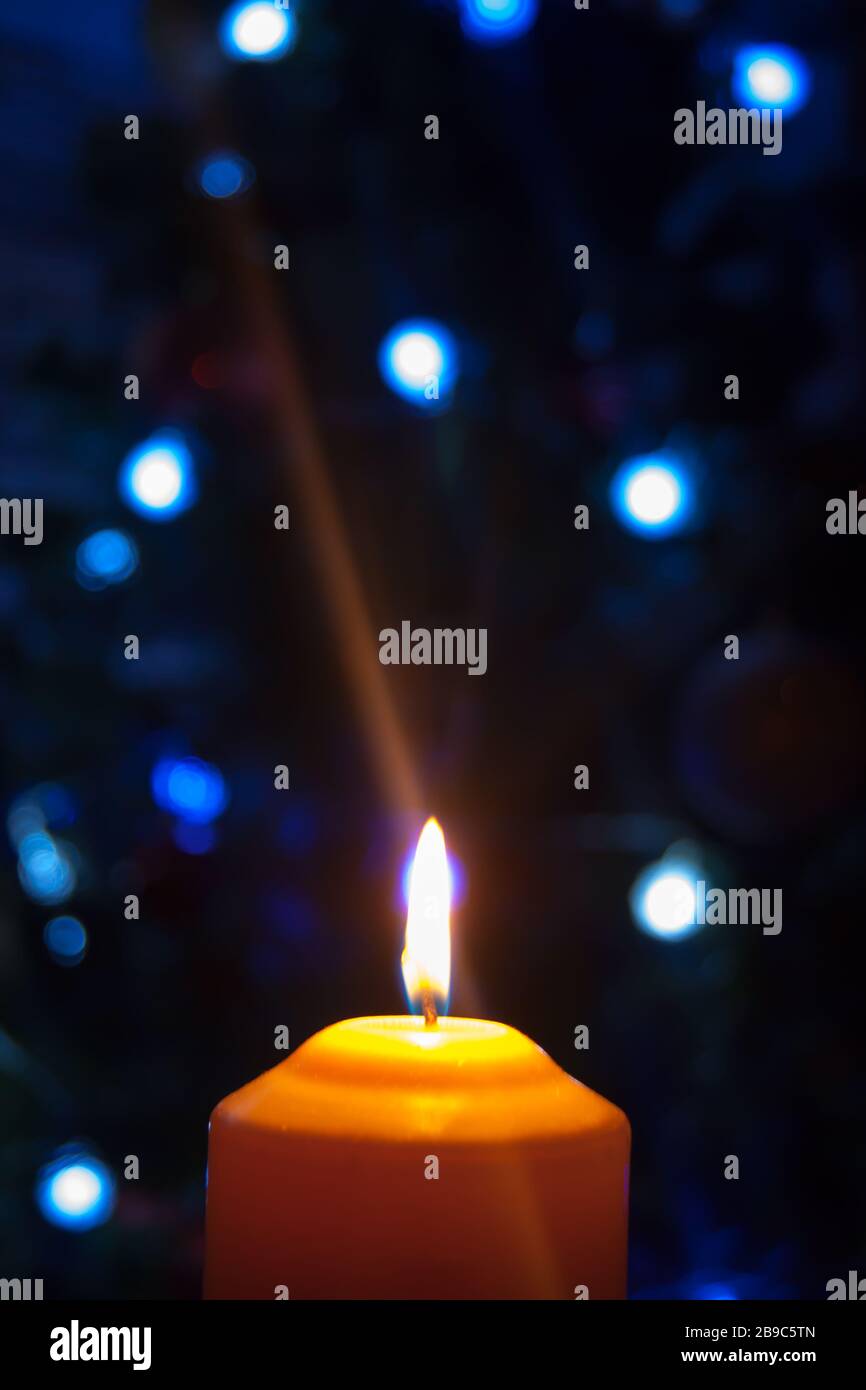 Eine große Kerze brennt vor dem Hintergrund einer Girlande mit strahlendem Licht. Vertikales Foto, Unschärfe. Mystische esoterische Romantik Divination Stimmung getauft Weihnachts-Karol-Setcer Stockfoto