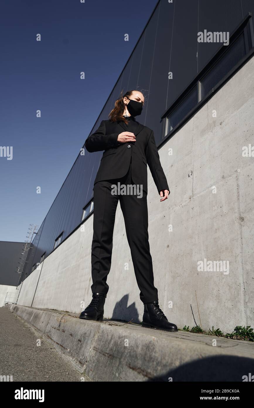 Ein junges Mädchen in einer schwarzen Virus-Schutzmaske in einem schwarzen Jackenkanzug auf der Straße. Mode während der viralen Bedrohung Stockfoto