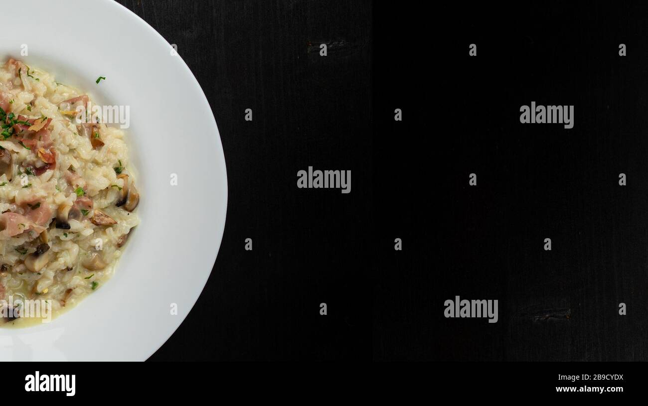 Super sauberes Täscher-Risotto mit Speck und Pilzen. Runde Platte und Holzhintergrund mit Platz für Text. Stockfoto