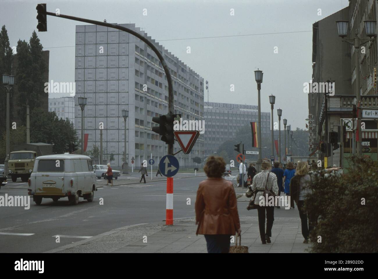 Fußgänger gehen über die Kreuzung Straße der Pariser Kommune / Karl-Marx-Allee, die mit DDR- und roten (sowjetischen) Flaggen dekoriert ist - im Hintergrund ist das Verlagsgebäude des neuen Deutschlands zu sehen. [Automatisierte Übersetzung] Stockfoto