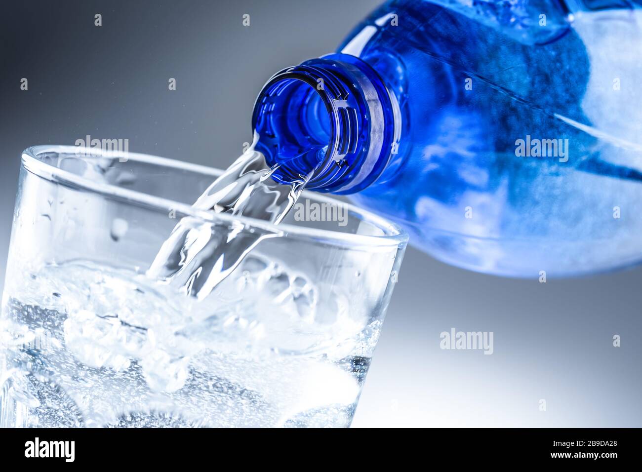 Mineralwasser aus blauer Flasche in klares Glas auf abstraktem grauem Hintergrund gießen Stockfoto