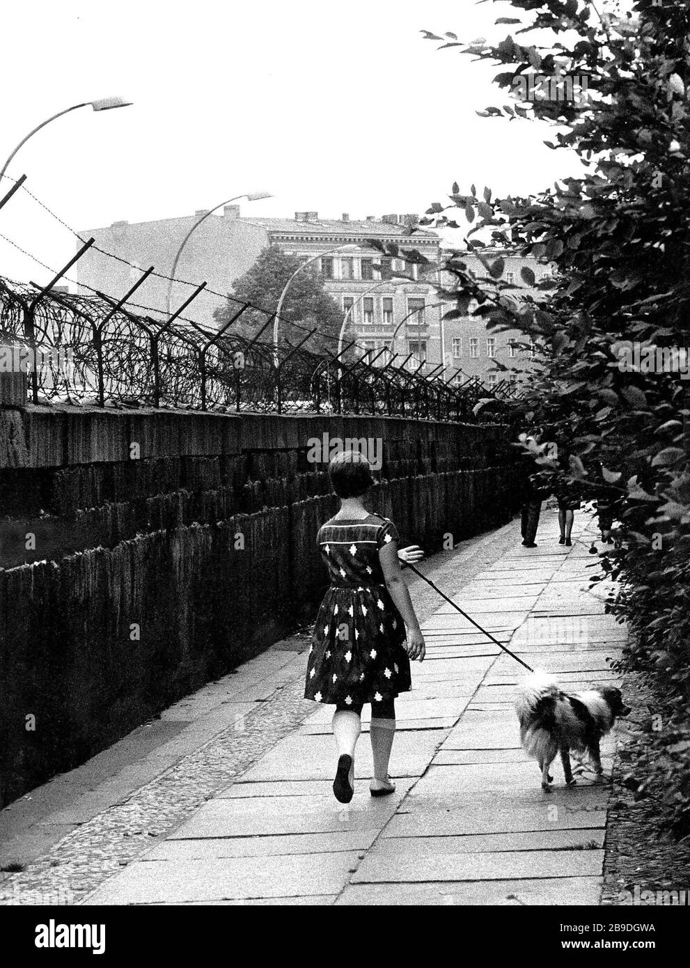 Ein Mädchen mit Kleid führt einen Hund an der Leine zu einem Spaziergang  entlang der Mauer in Berlin. [Automatisierte Übersetzung] Stockfotografie -  Alamy