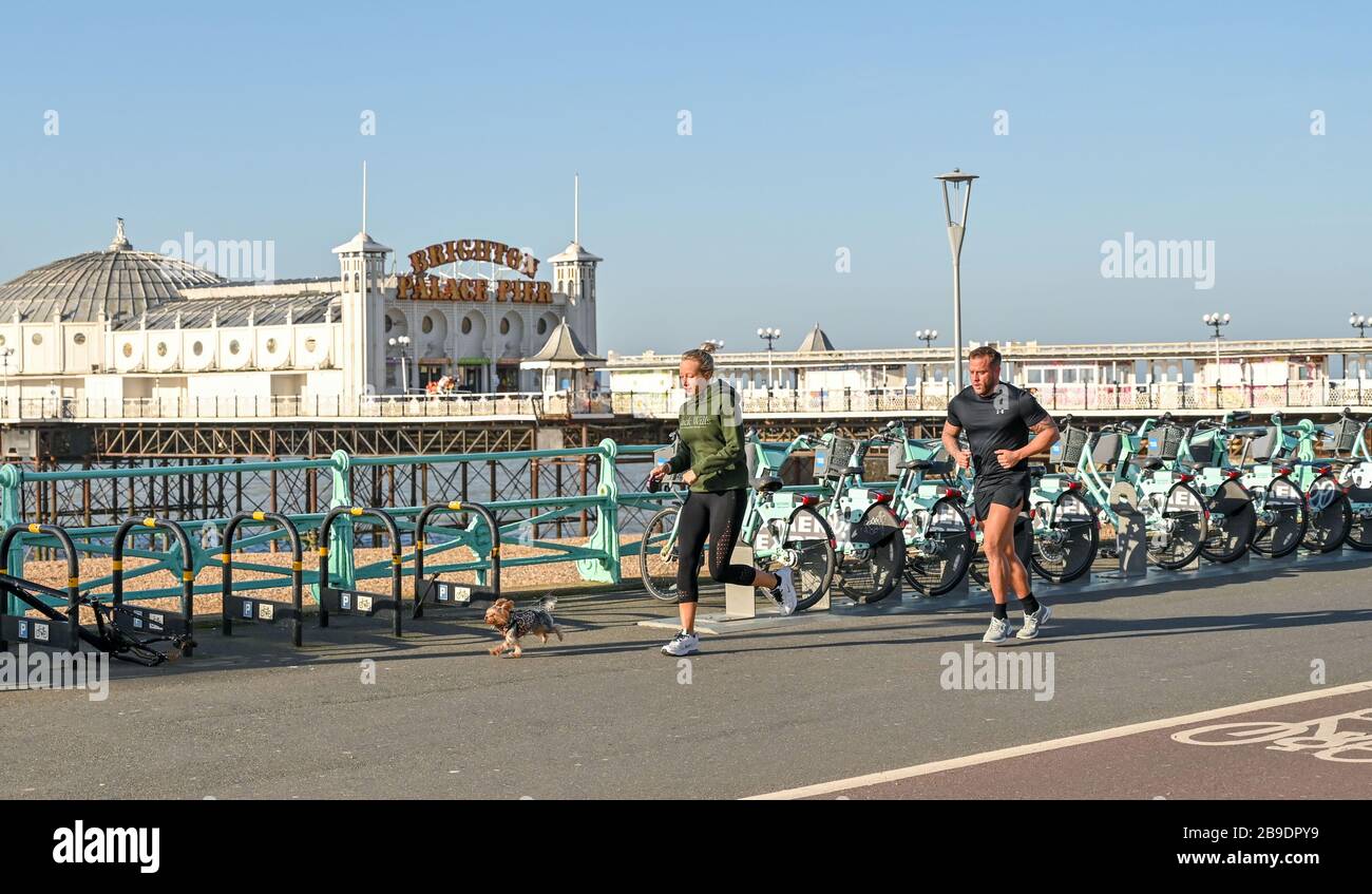 Brighton UK 24. März 2020 - Läufer mit ihrem Hund, die an einem schönen sonnigen Morgen an der Küste von Brighton trainieren, während die neuen staatlichen Einschränkungen während der Coronavirus COVID-19-Pandemie-Krise auftreten. Kredit: Simon Dack / Alamy Live News Stockfoto