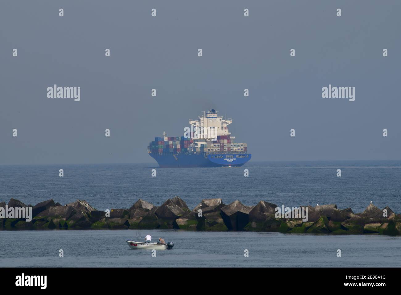 Riesige Containership verlässt den Hafen von Rotterdam auf die Nordsee mit tw0-Fischer in einem kleinen Beiboot im Vordergrund Stockfoto