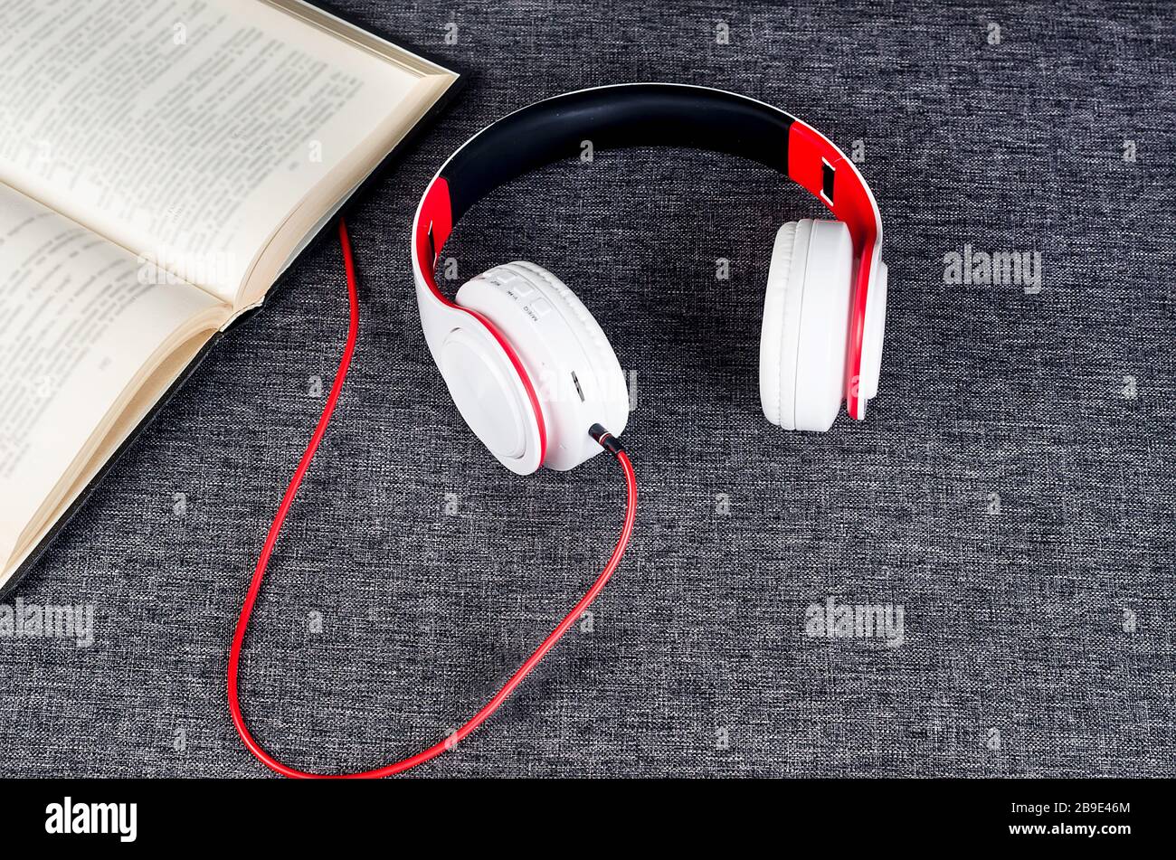 Offenes Buch mit Kopfhörern auf grauem Sofa. Audiobuchkonzept: Moderne Bildung, Lesen. Hörbücher, Podcasts und Online-Kurse anhören. Stockfoto