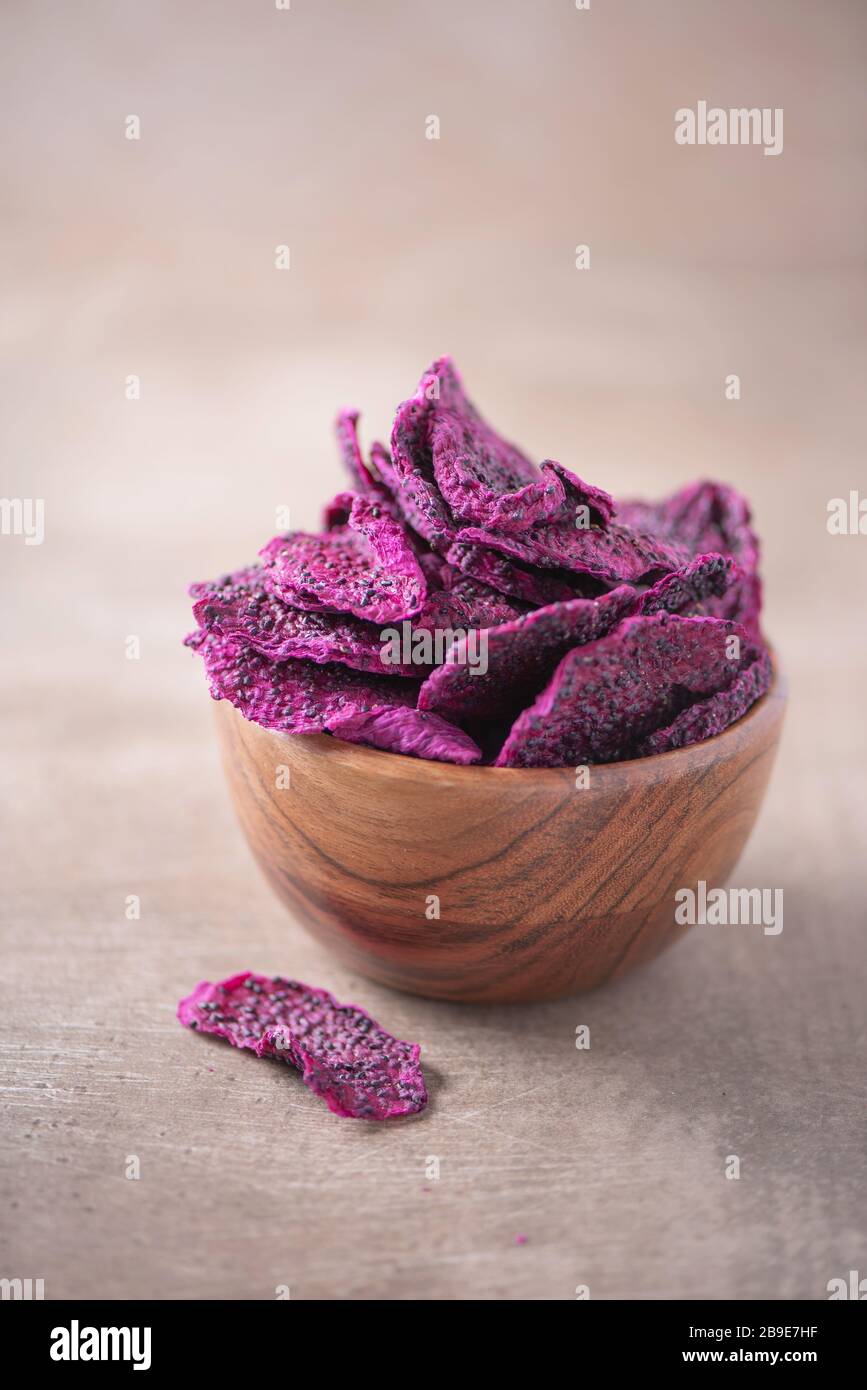 Getrocknete Scheiben von rosafarbenen Drachenfrüchten, Pitaya in Holzschale auf strukturiertem Holzhintergrund. Kopierbereich. Superfood, veganes, vegetarisches Speisekonzept. Makro von Stockfoto